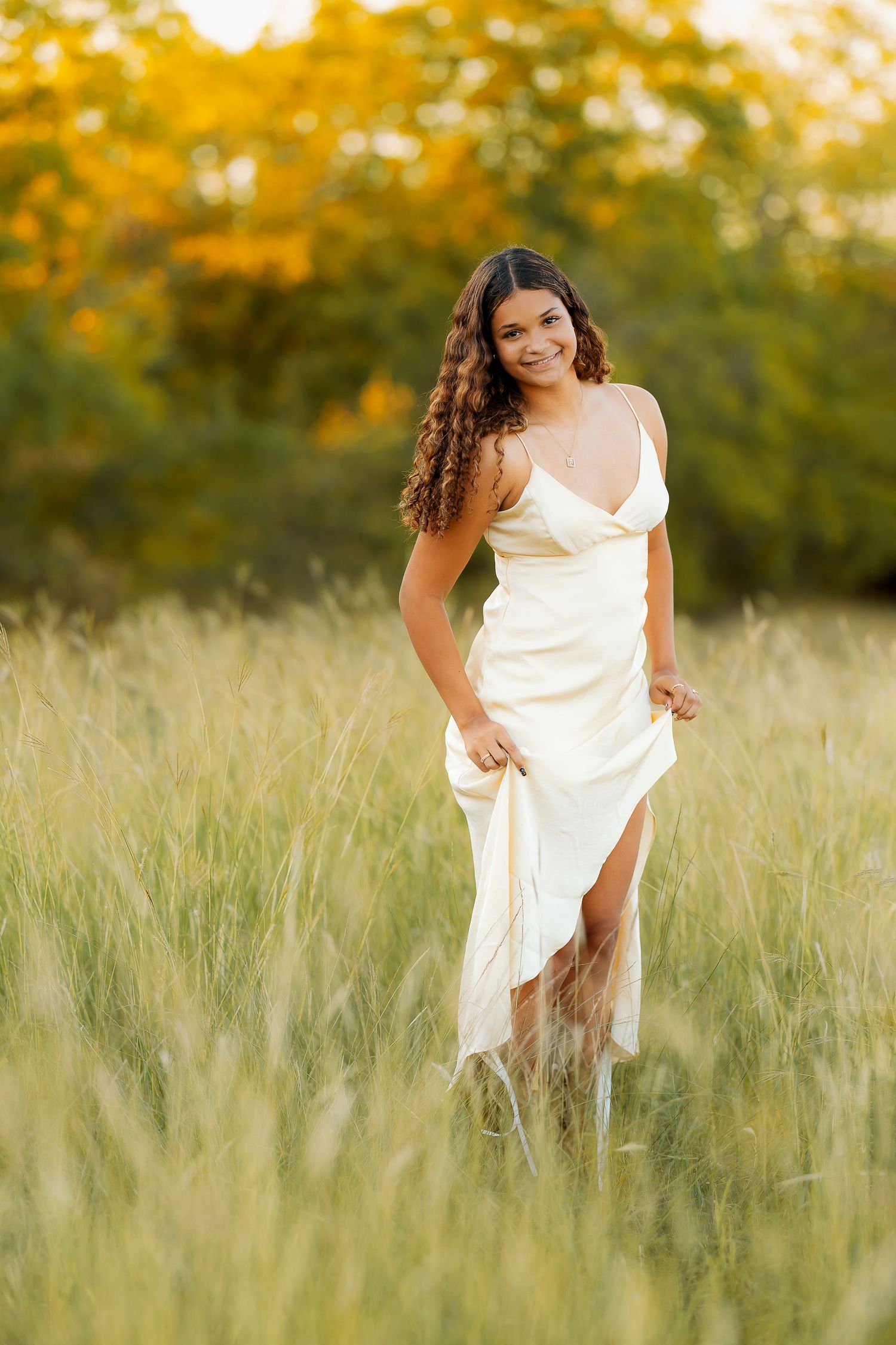 Senior photos flowing white dress poses in tall grass during sunset. Natural settings in summer - Frisco Texas.
