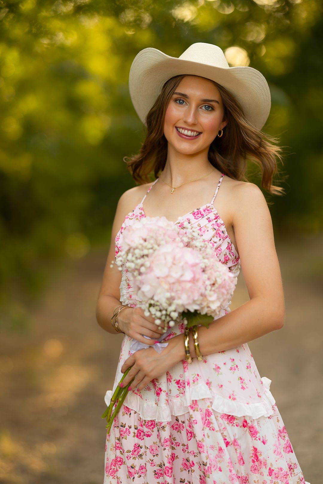 Outdoor portraits in floral dress and cowboy hat holding pink and white flowers.