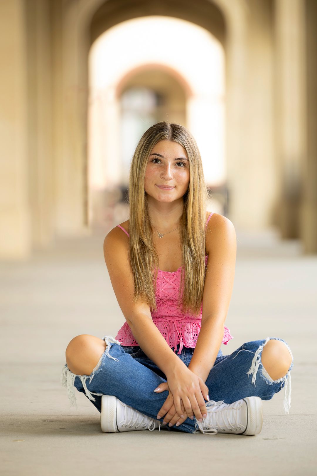Casual portrait in pink top and jeans sitting on floor with natural lighting.