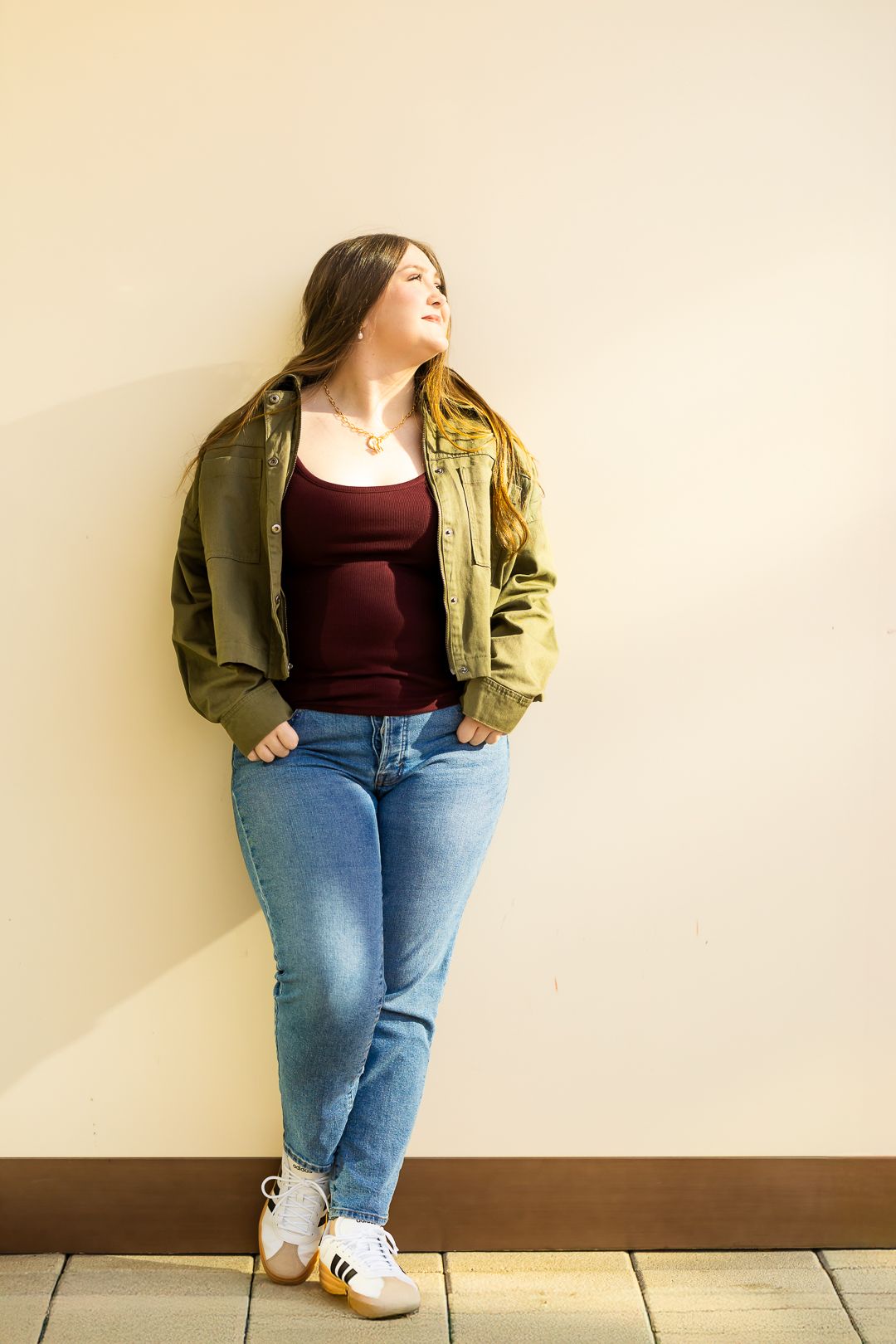 Casual outfit featuring blue jeans, burgundy top and olive green jacket paired with white sneakers.