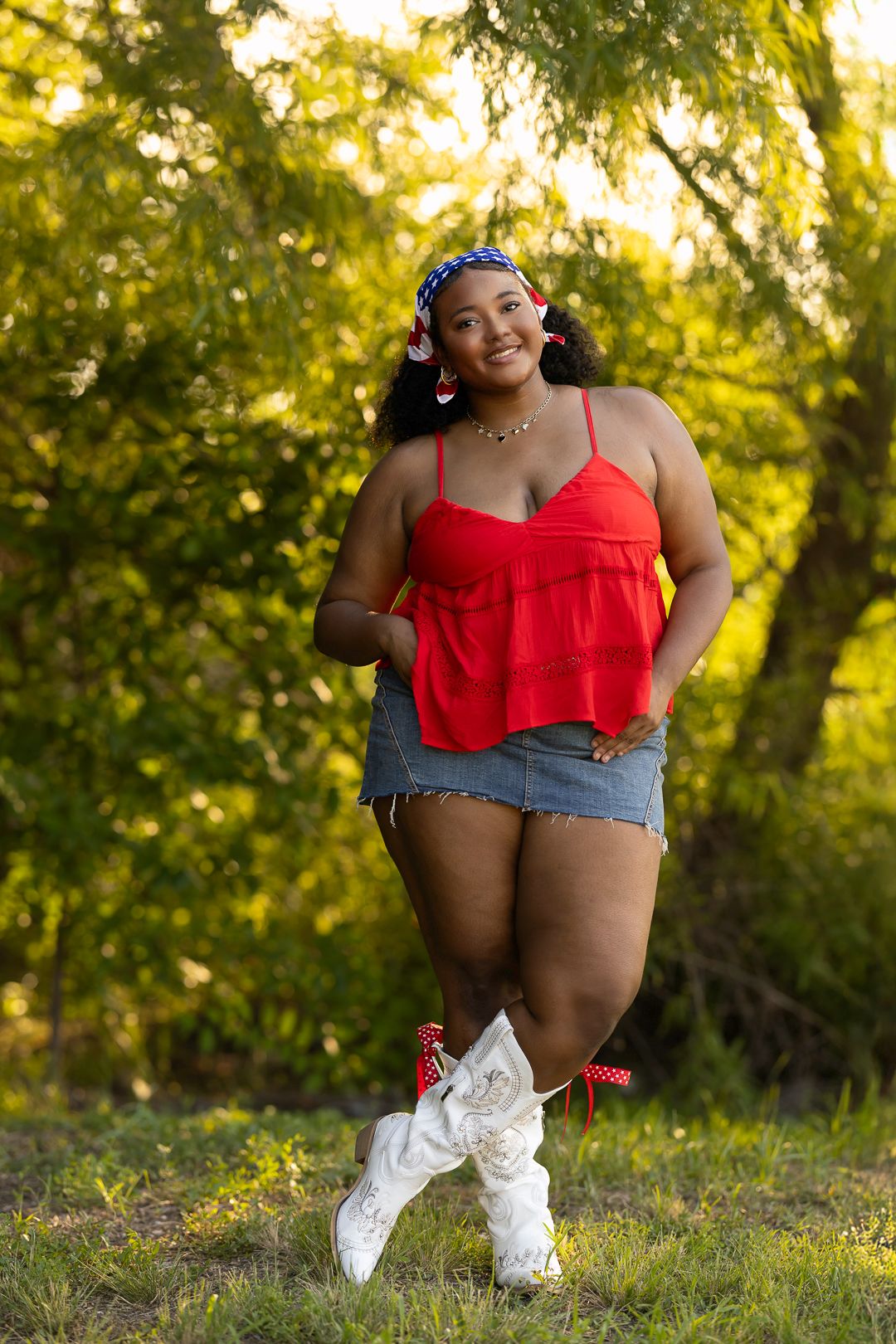 A person in a red top and denim shorts sits in grass during golden hour sunset lighting.