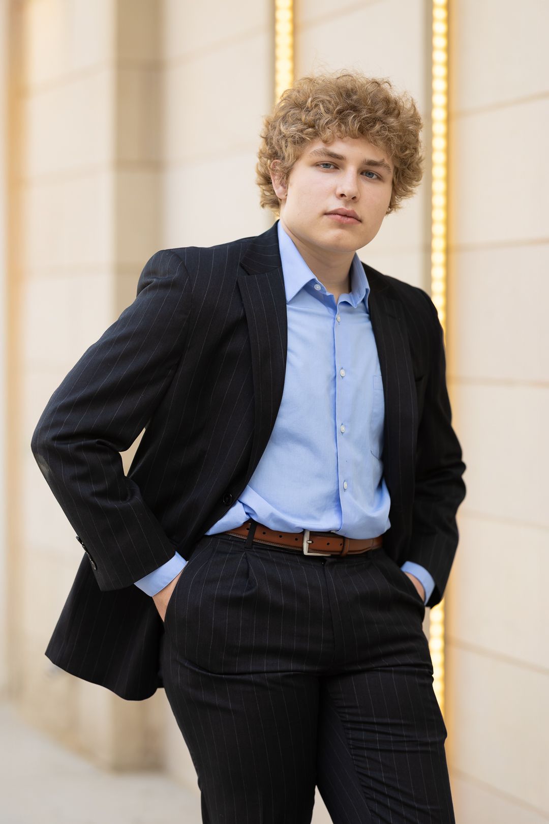 A person in a black pinstripe suit and light blue shirt poses against a light-colored wall in three similar poses.