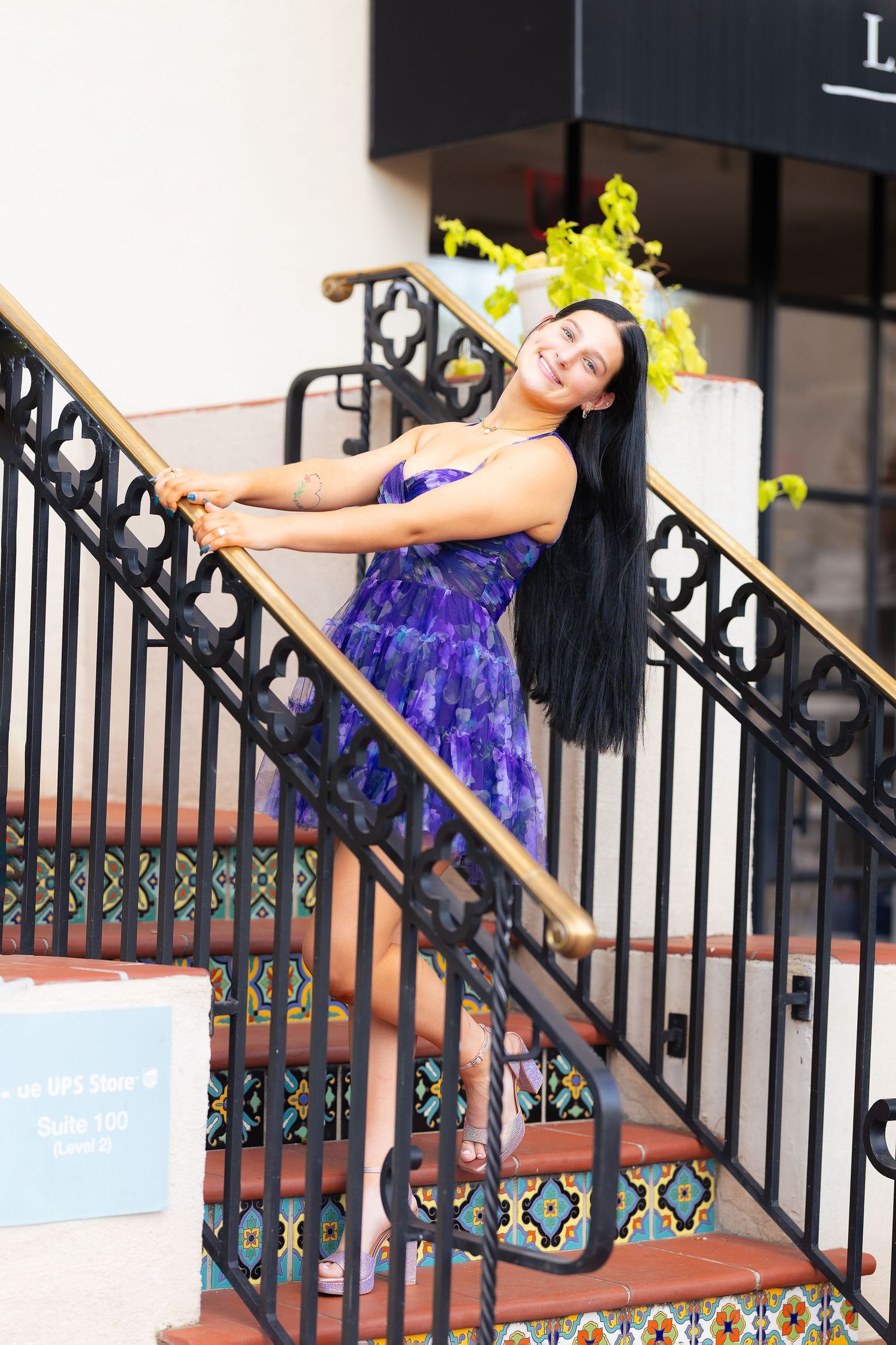 Dancer in purple dress performs graceful pose while leaning on outdoor staircase railing.