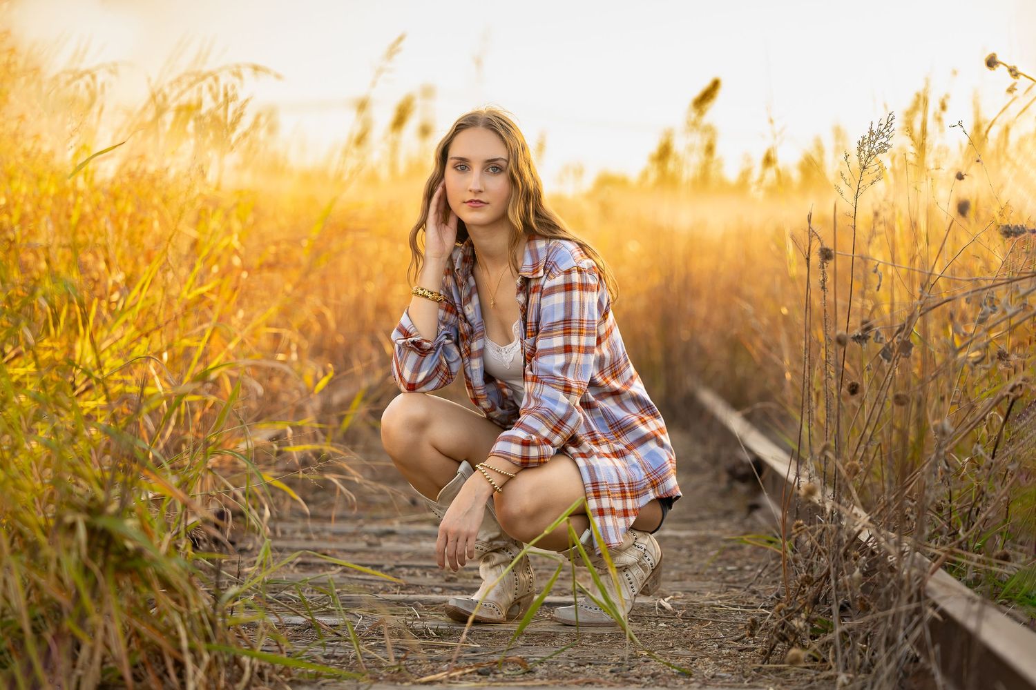 A person in plaid shirt poses in golden wheat field during sunset creating a warm autumn aesthetic.