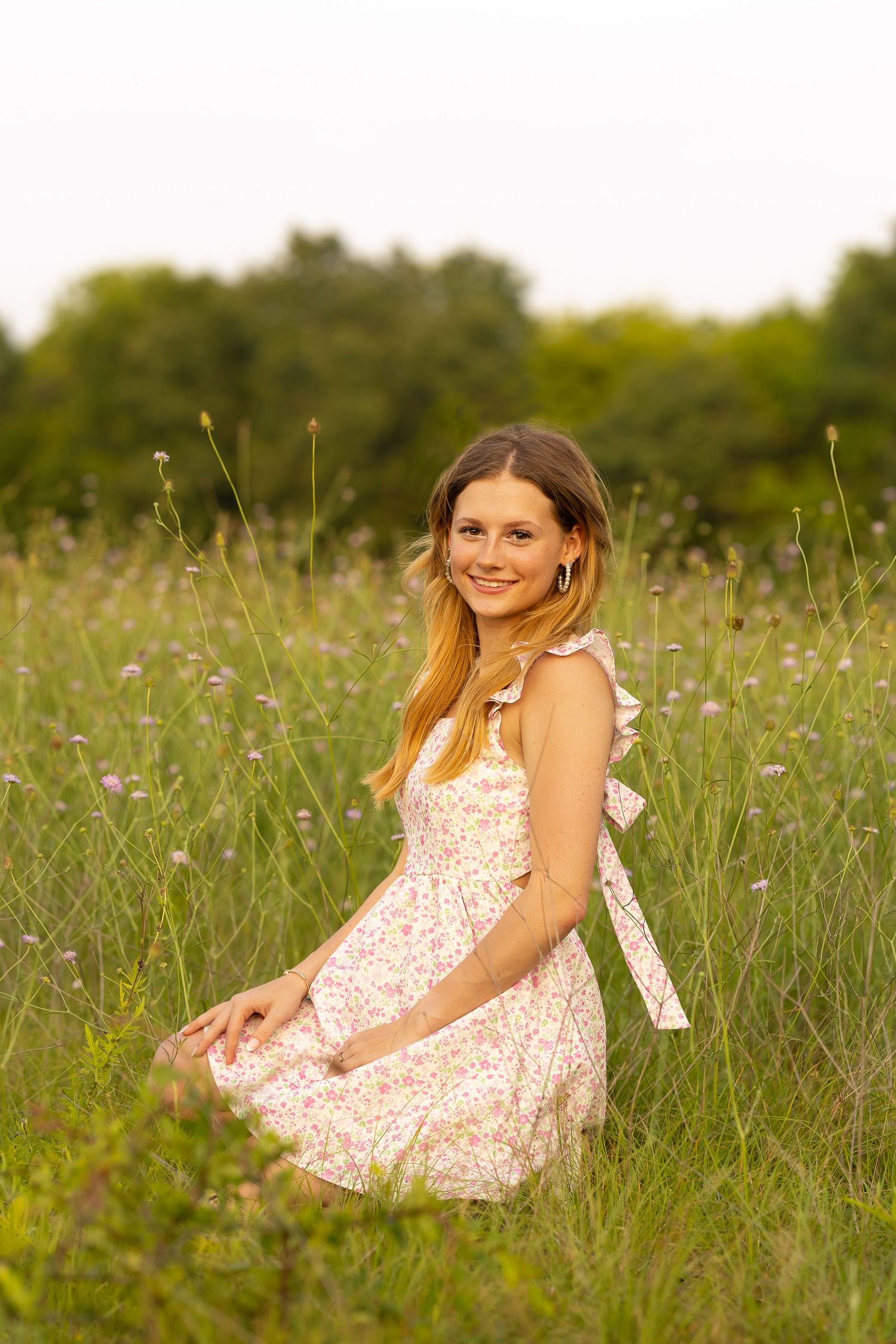 A person in a floral sundress sits gracefully in a wildflower meadow during golden hour.