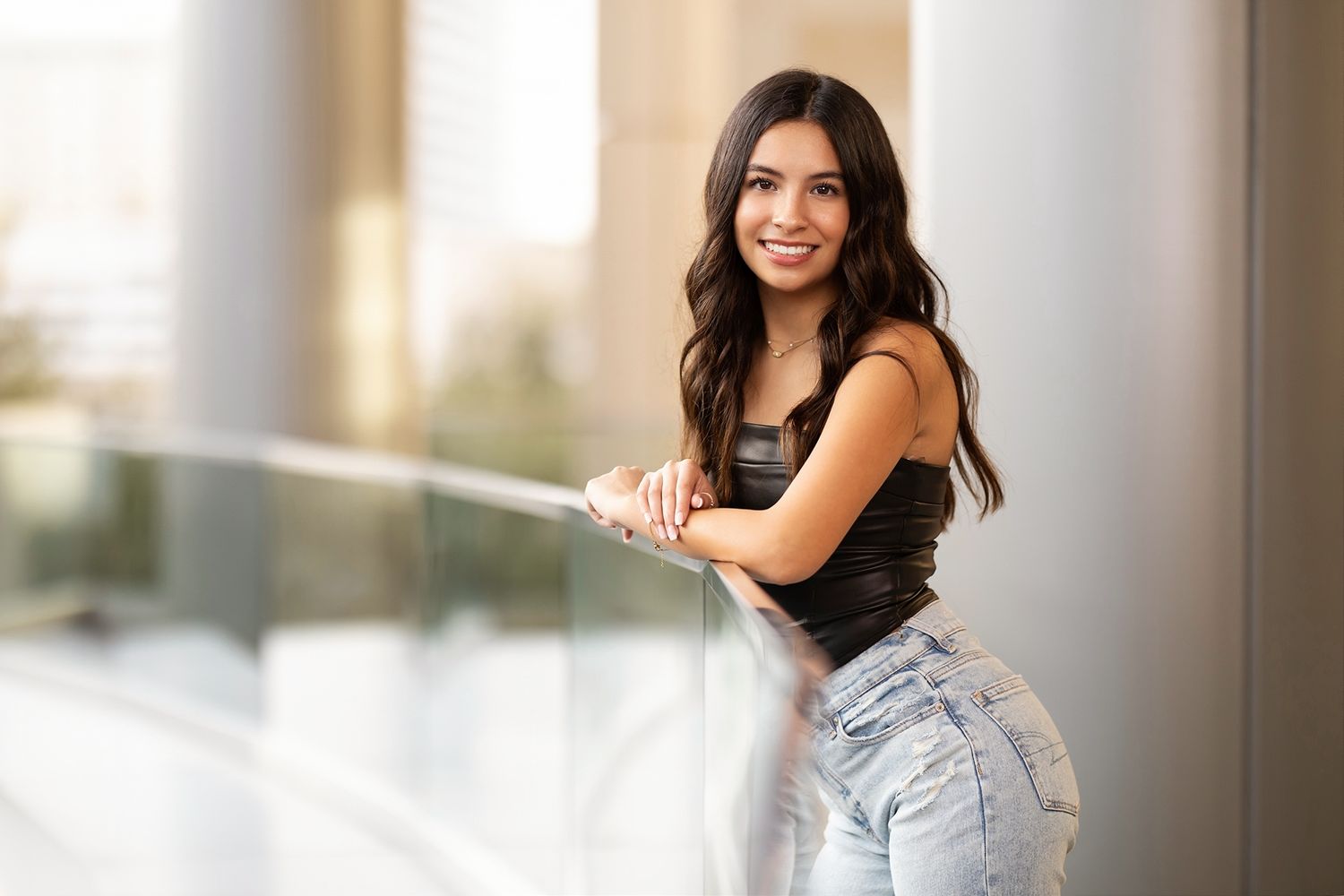 A woman poses elegantly against a bright interior wall wearing a white dress.