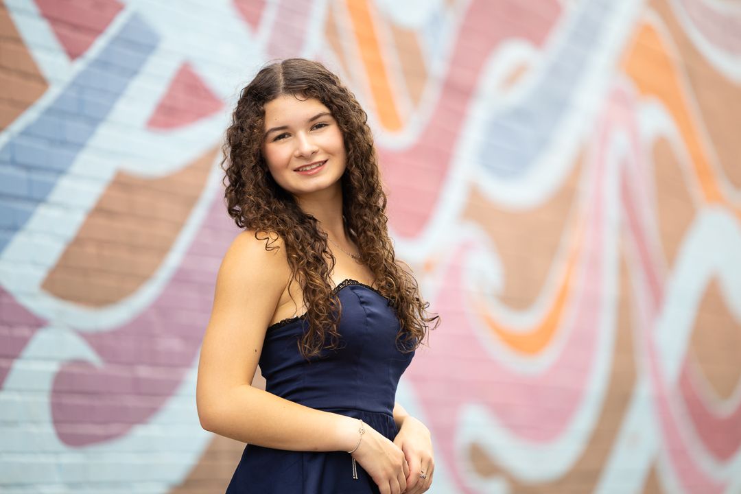 A person in a navy blue dress poses for portraits against a colorful graffiti wall background.