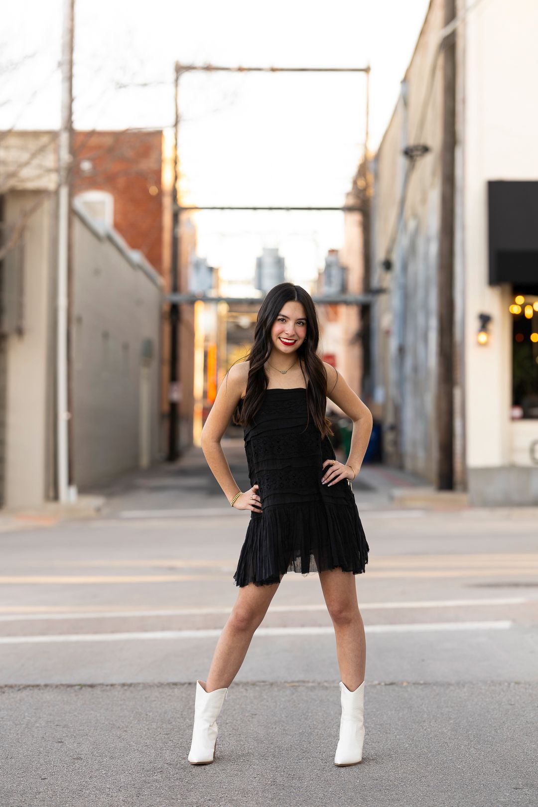 Person in black dress poses playfully near white columns.