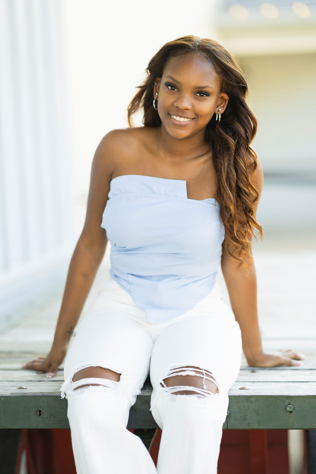 Someone in light blue and white sits casually on a wooden deck.