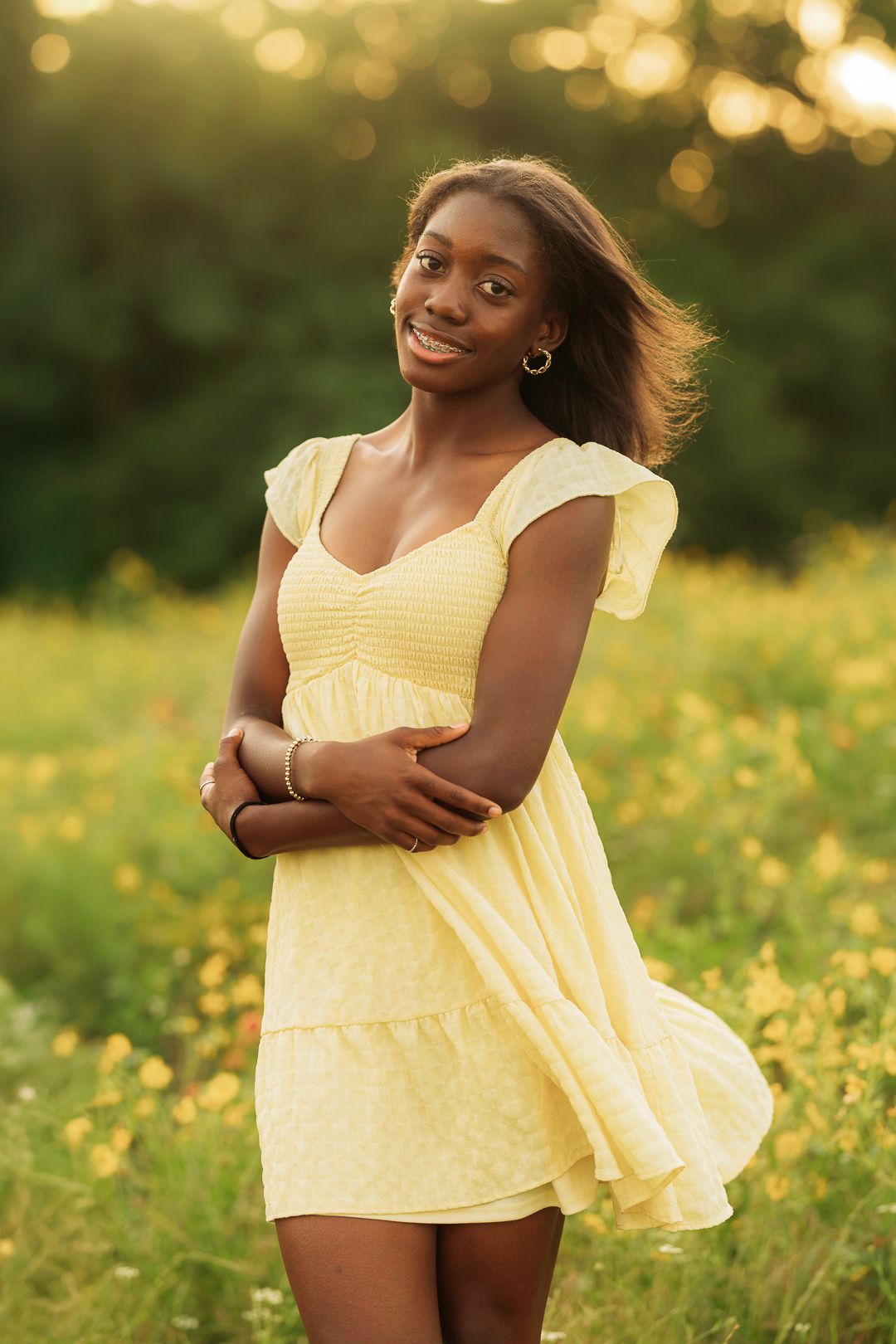 Young Black woman in yellow sundress smiling in golden hour sunlit wildflower field.