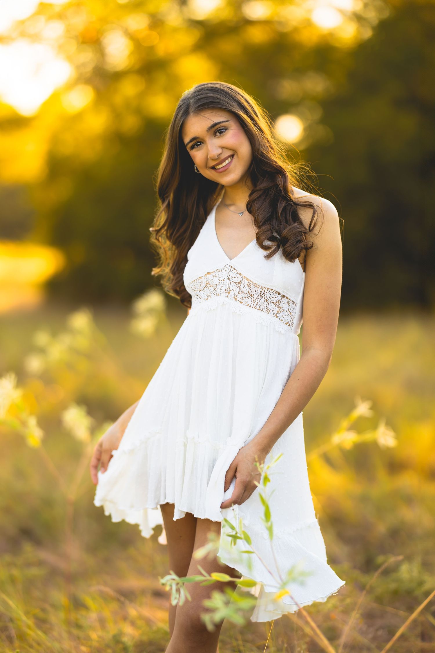 A white lace dress flows gracefully in a golden sunlit field during a summer portrait session.