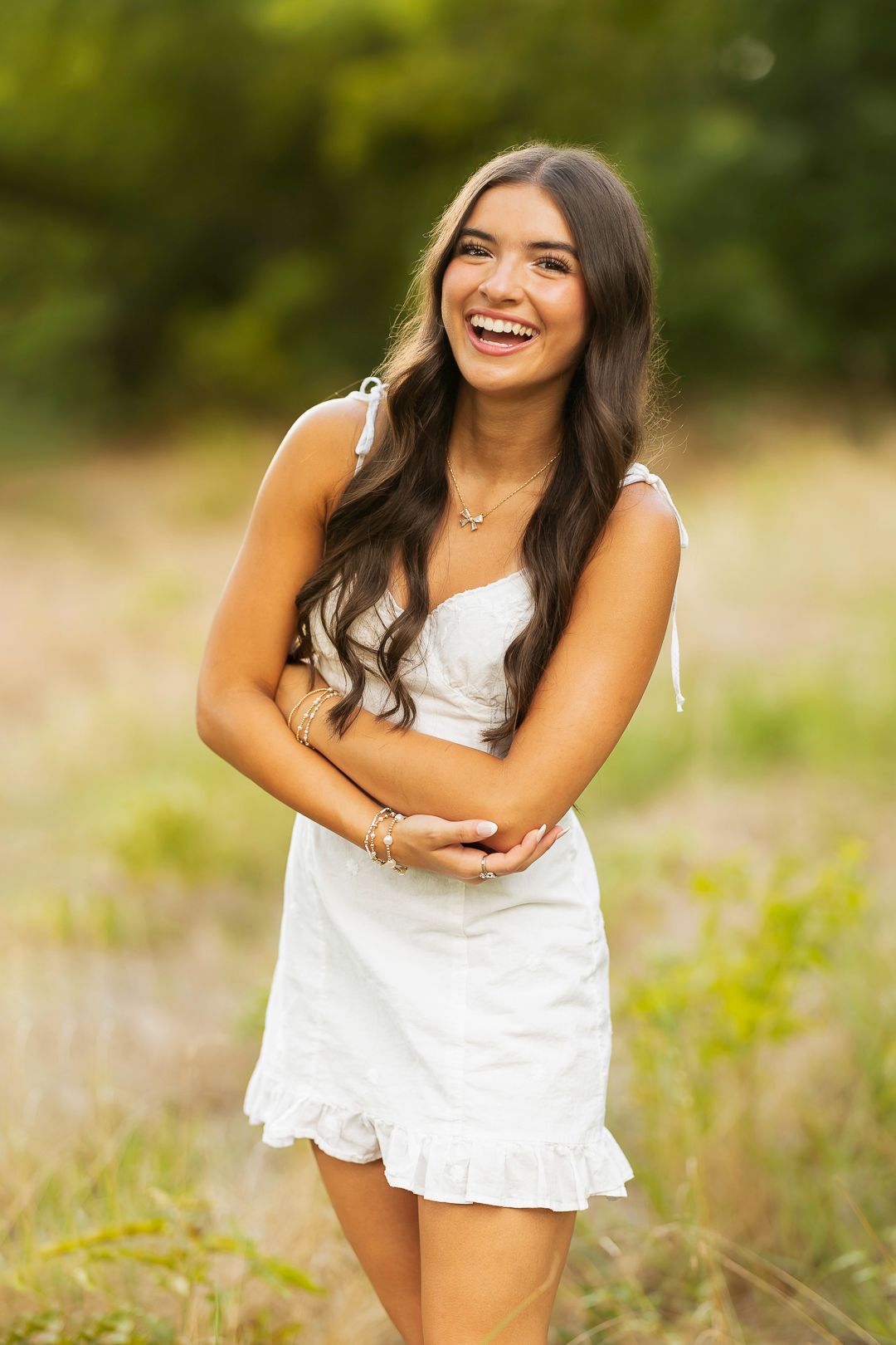 Fun senior pictures in a white ruffled dress.  natural grassy background.