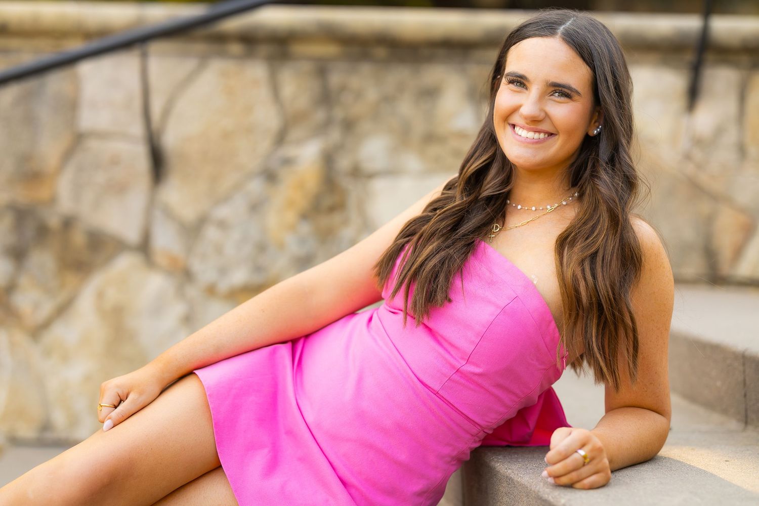 Woman in bright pink dress poses elegantly on stone steps.