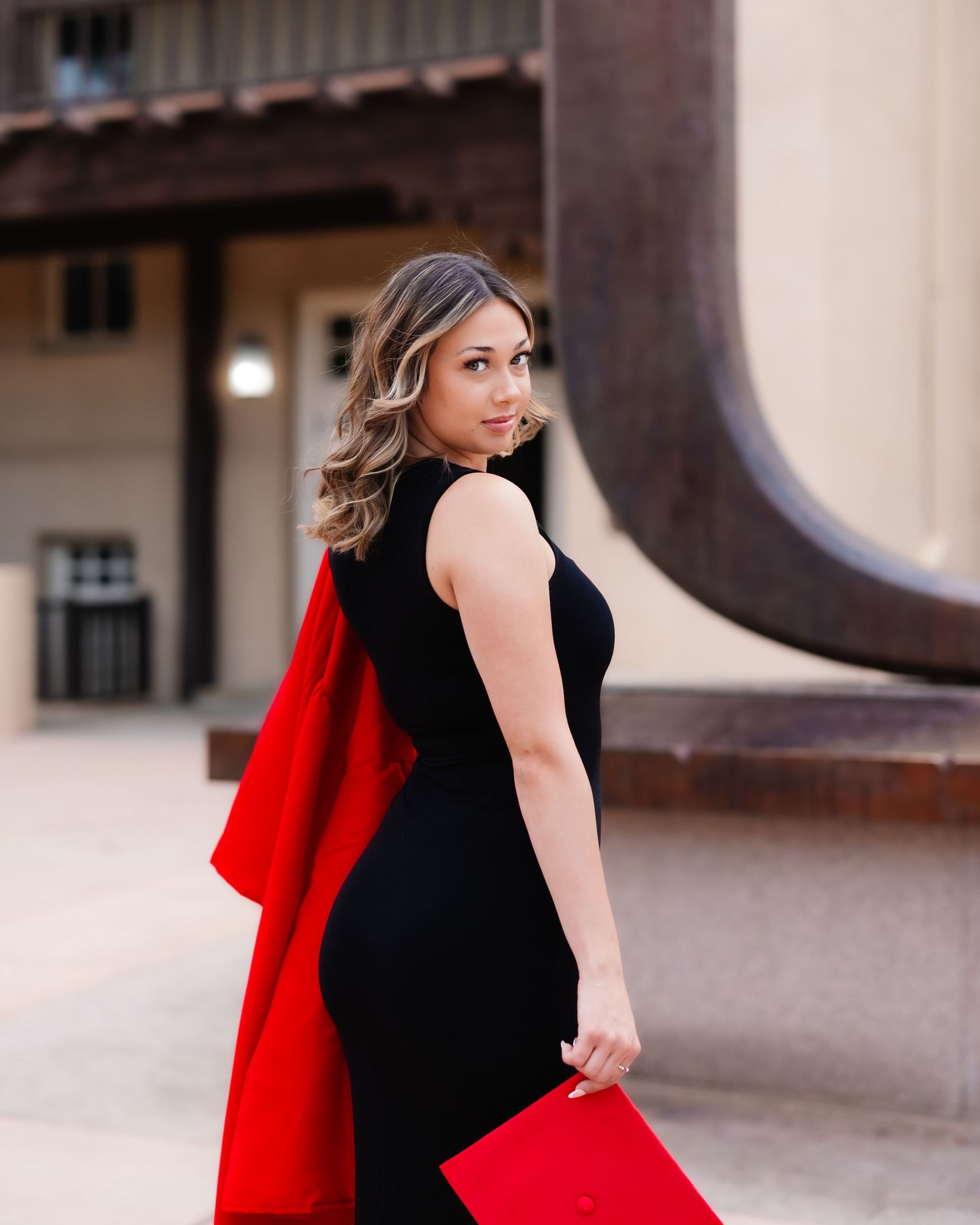 A woman in a black dress poses with a flowing red cape against an architectural backdrop.
