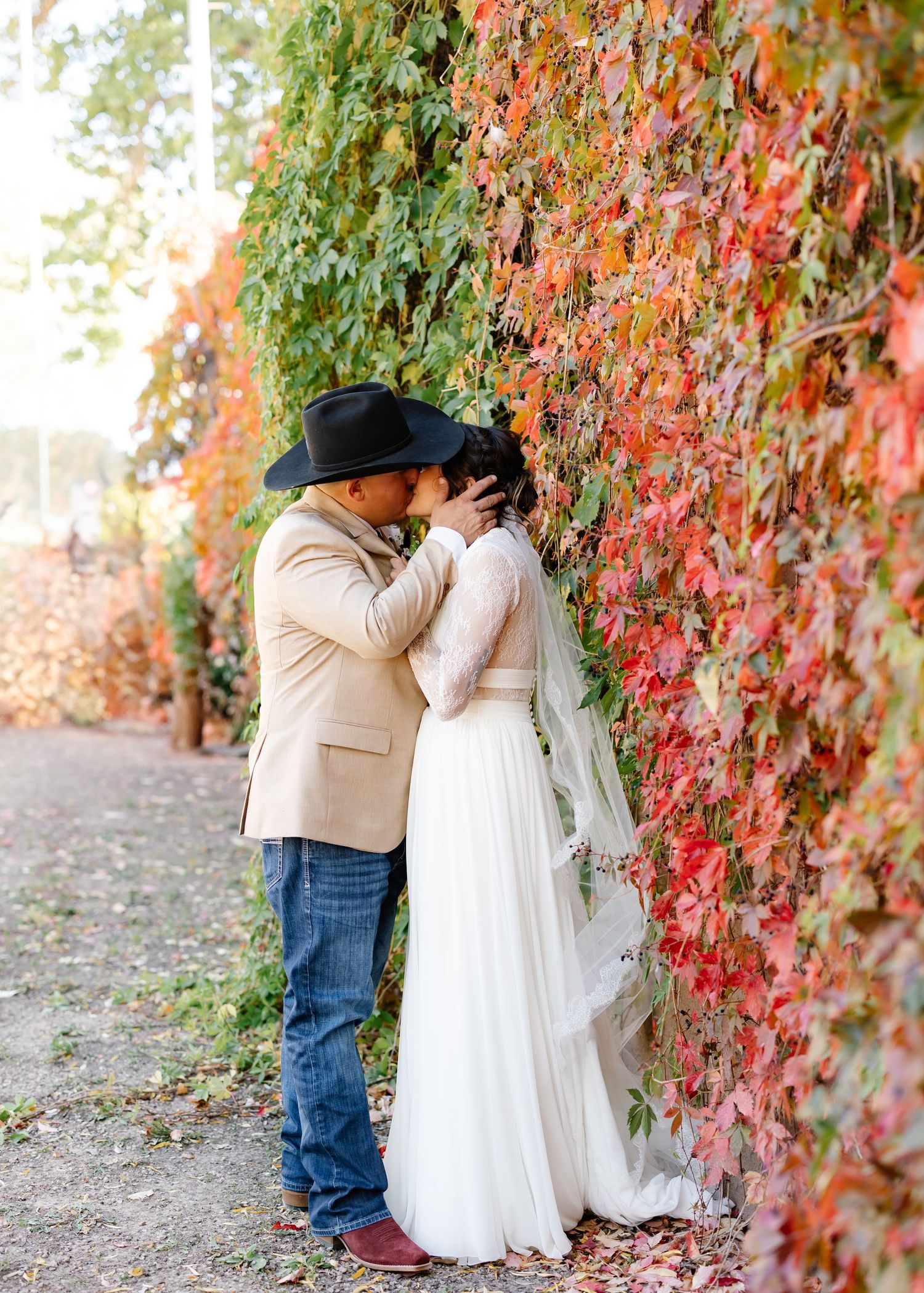 Romantic wedding couple shares sweet kisses under vibrant red autumn vines along a stone wall.