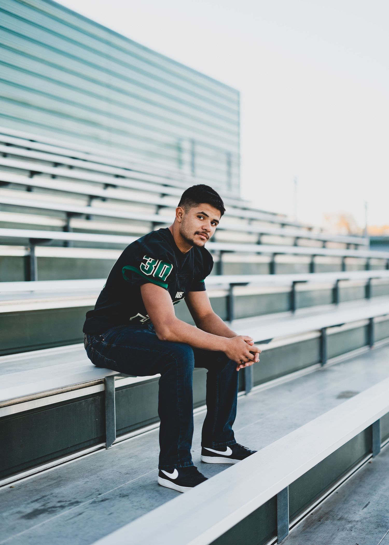 A person in casual attire sits contemplatively on empty stadium bleachers.