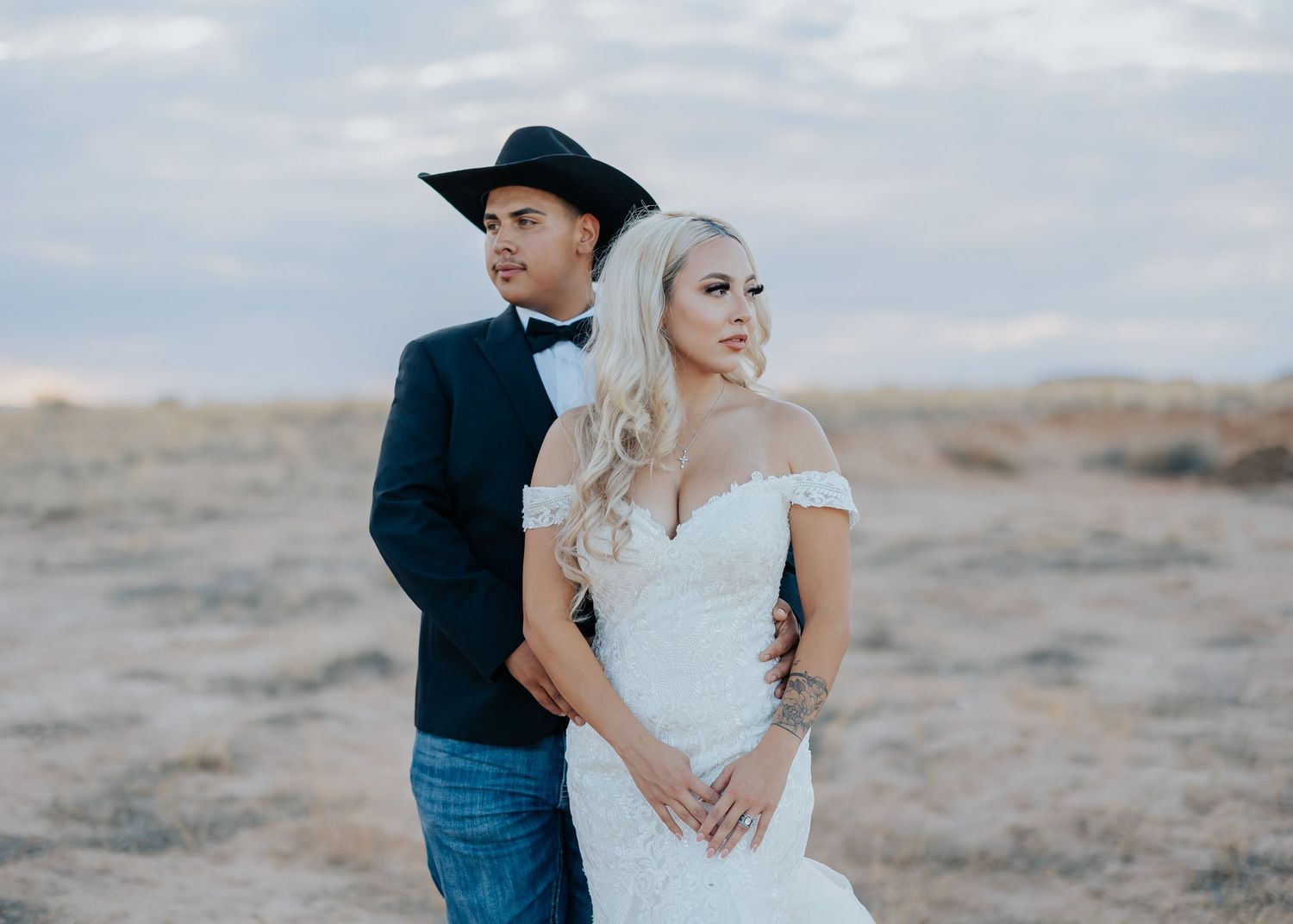 Couple embracing in a desert landscape with a moody cloudy sky backdrop.