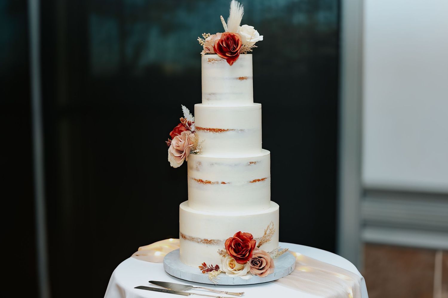 Five tall white wedding cakes with rustic styling and burgundy floral decorations displayed in a row.