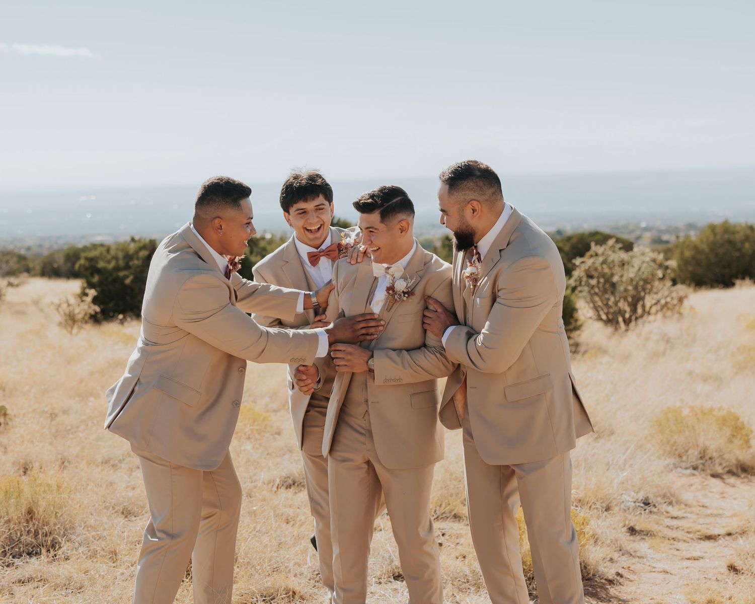 Groomsmen in khaki suits sharing a laugh in a desert setting.