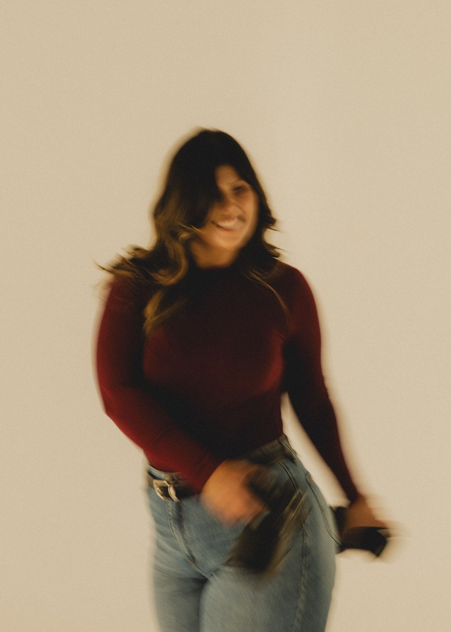 Figure in burgundy sweater and jeans performs expressive dance movements against neutral background in motion blur sequence.
