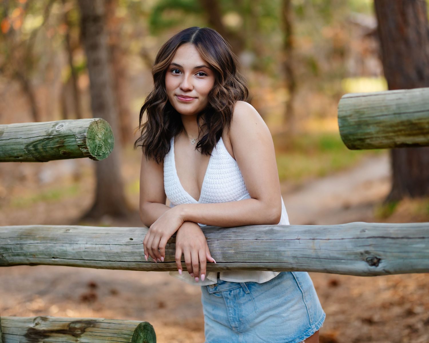 A casual portrait against wooden fence rails in an autumn forest setting.