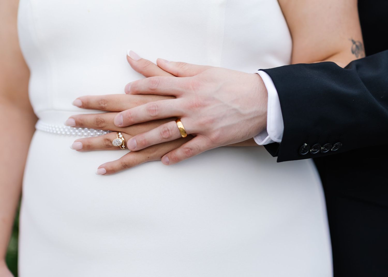 Detail shot of hands with wedding rings against white dress fabric.