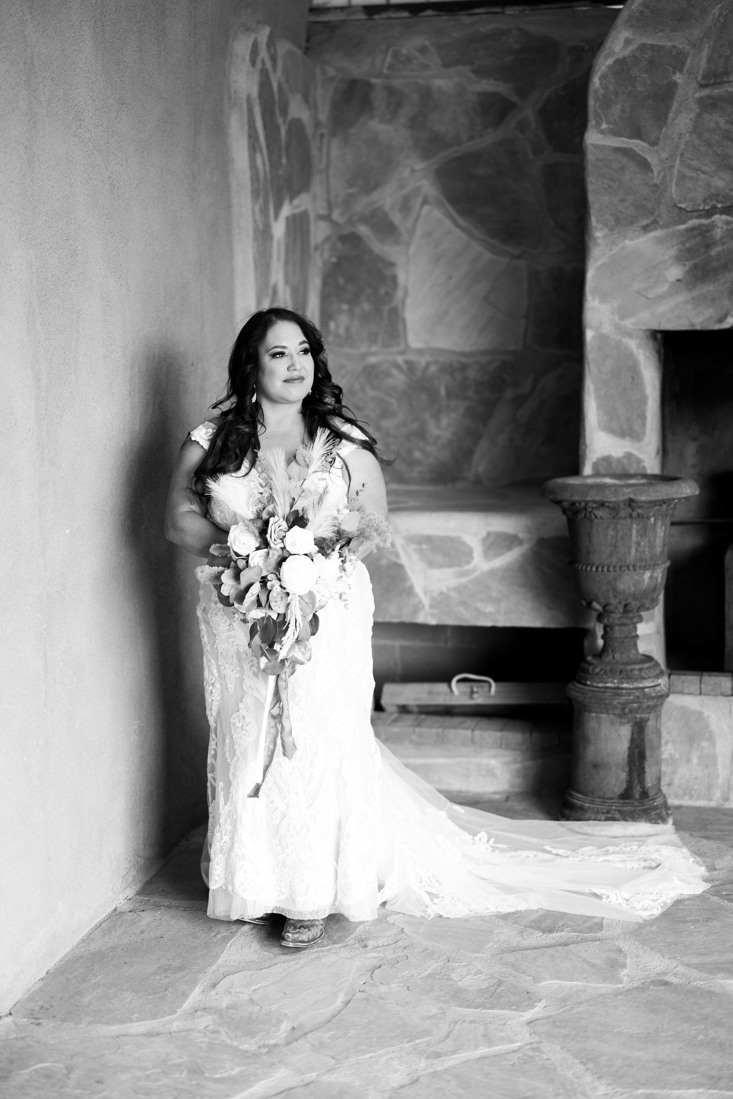 A figure in a flowing white dress poses dramatically in a stone archway corridor in black and white photography.