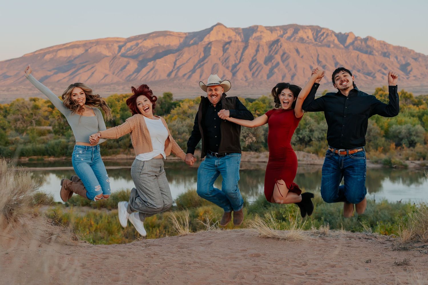 Group of friends jumping in unison with Sandia Mountains and desert landscape in background.