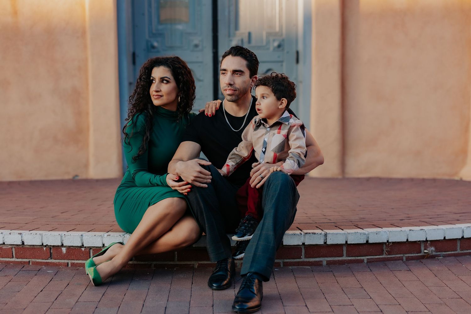 A family sits together on brick steps in front of a traditional southwestern blue door.