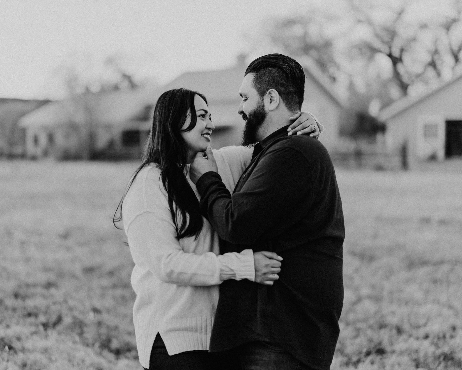 Black and white photo of a loving couple embracing and smiling at each other in an outdoor field setting.