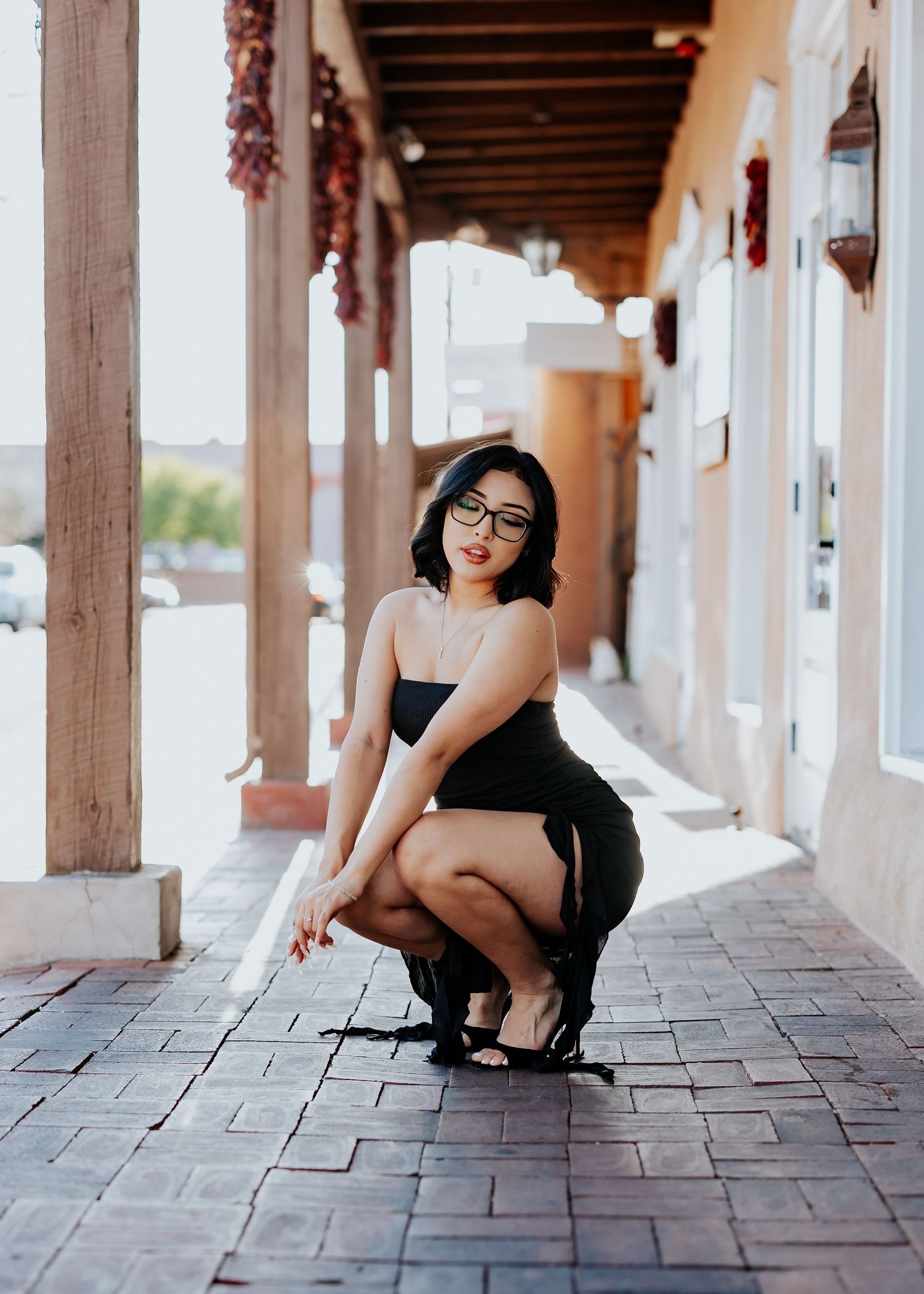 A woman in black poses in a traditional Southwestern covered walkway with wooden beams.