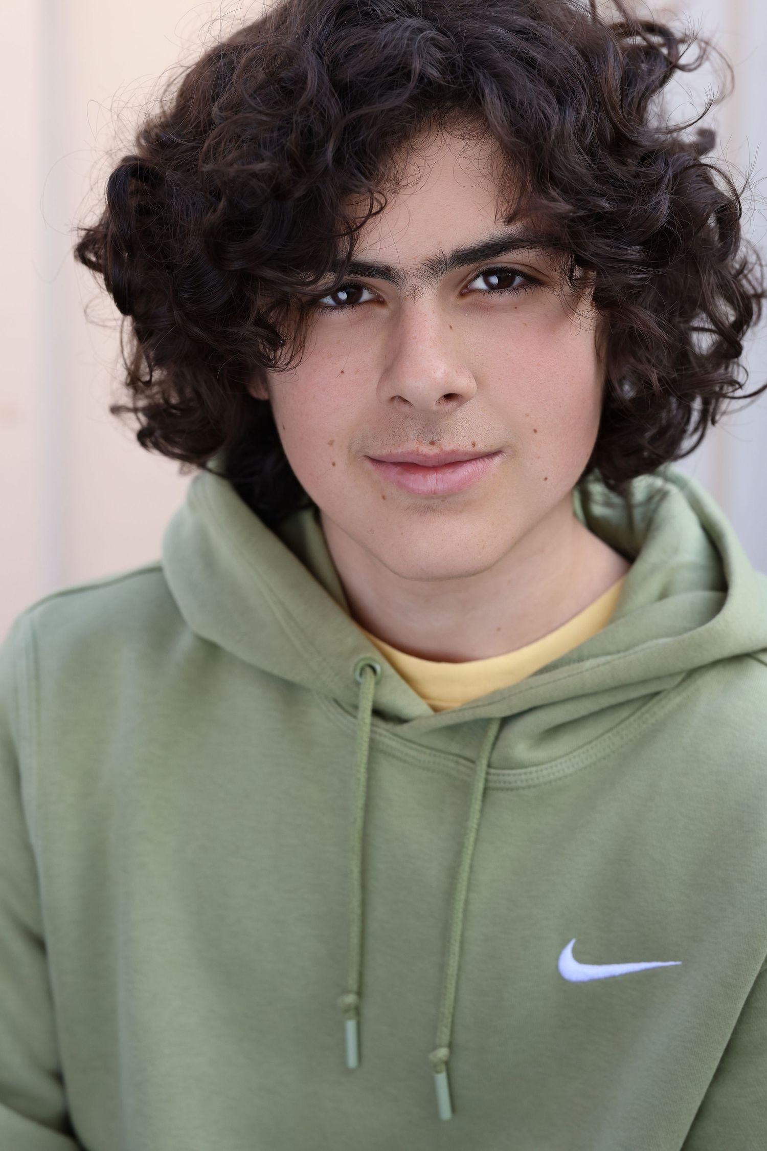Person with curly dark hair wearing a light green Nike hoodie smiles in a series of four similar headshots.
