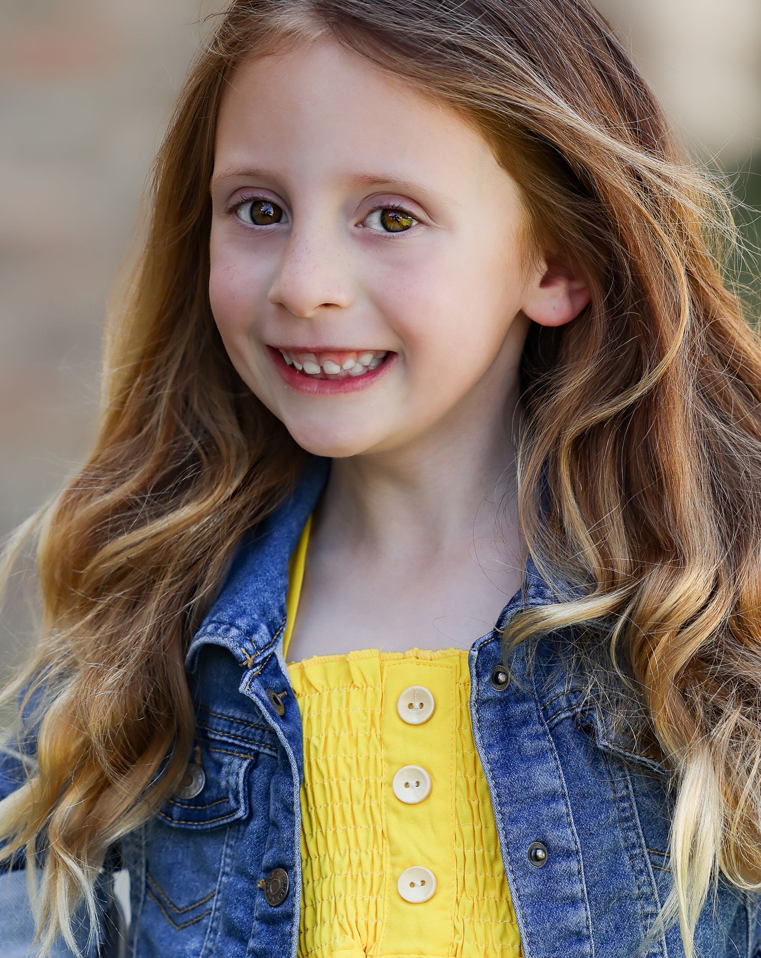 Cheerful headshot in denim jacket and yellow top with flowing hair.