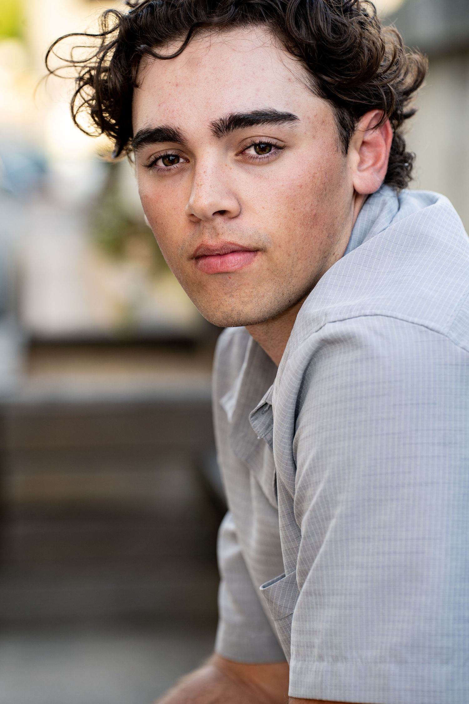 A person in a light gray collared shirt poses against a blurred background in a series of similar headshots.