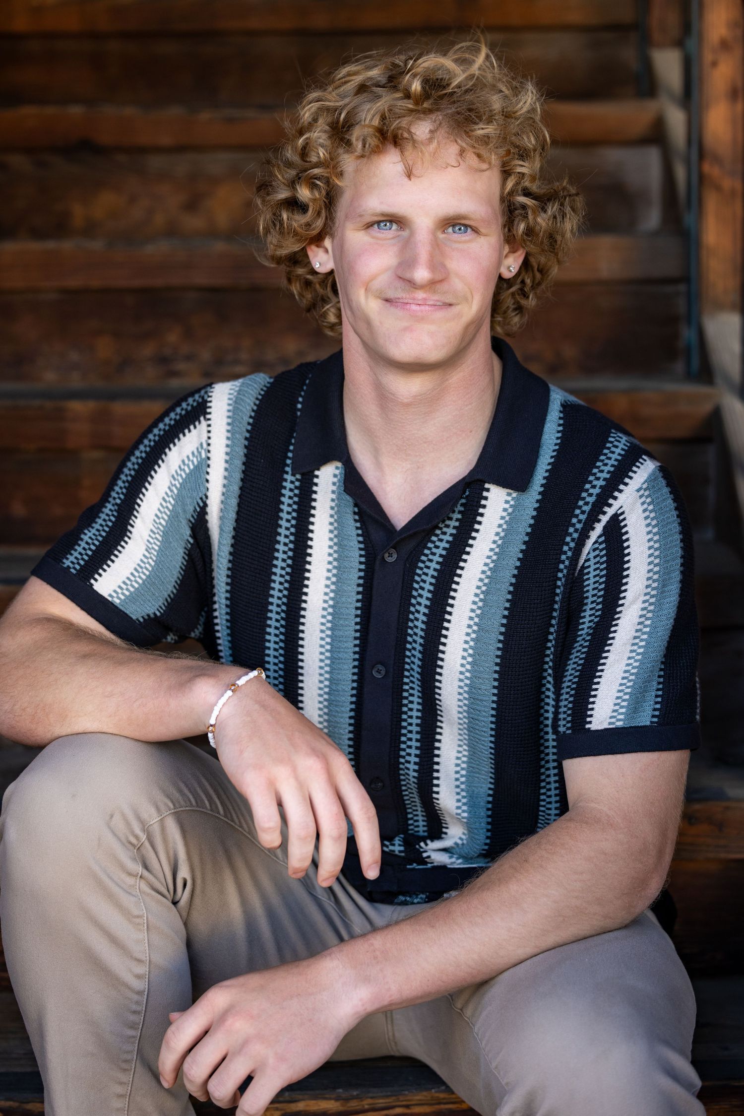 male actor headshot series in striped navy sweater against rustic wooden wall backdrop.