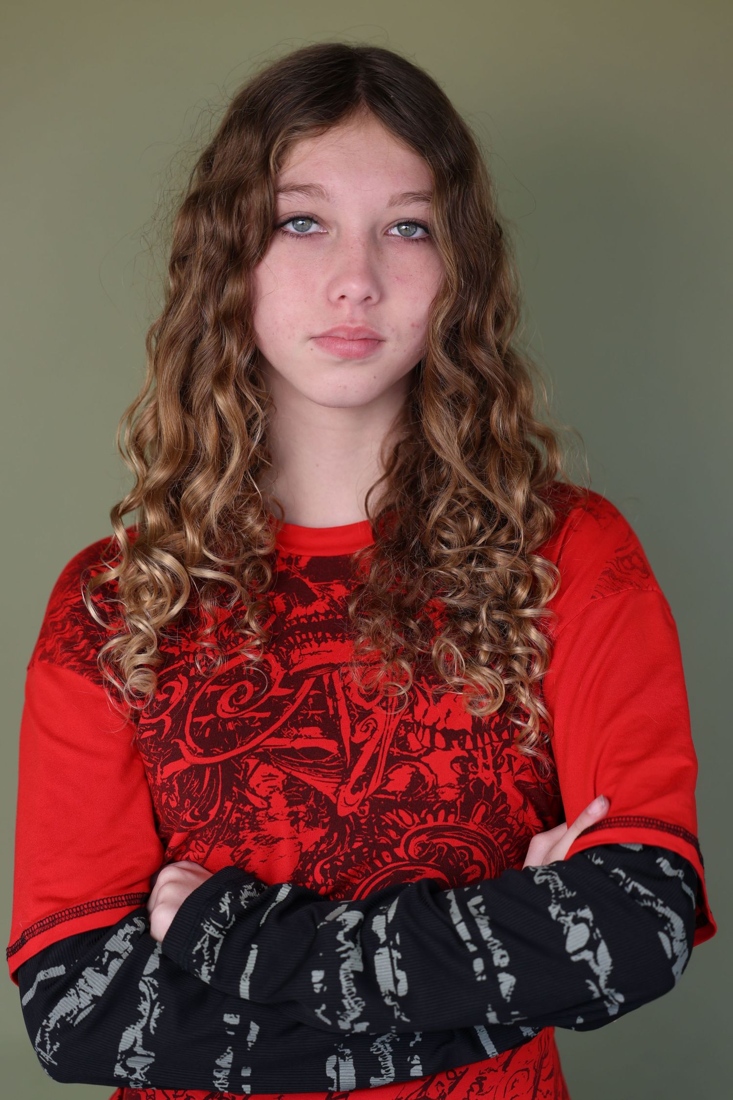 goth girl headshot. Casual pose in red and black graphic sweatshirt with wavy hair.