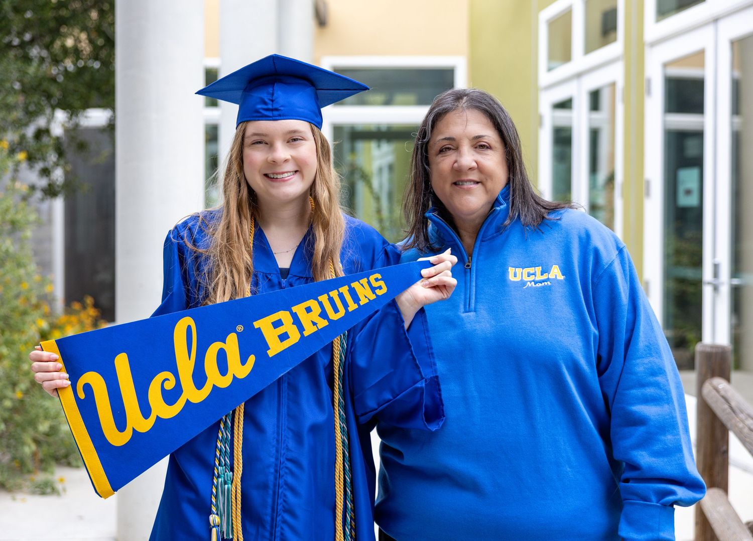 A group wearing bright blue graduation gowns and caps poses together outdoors in front of a building.