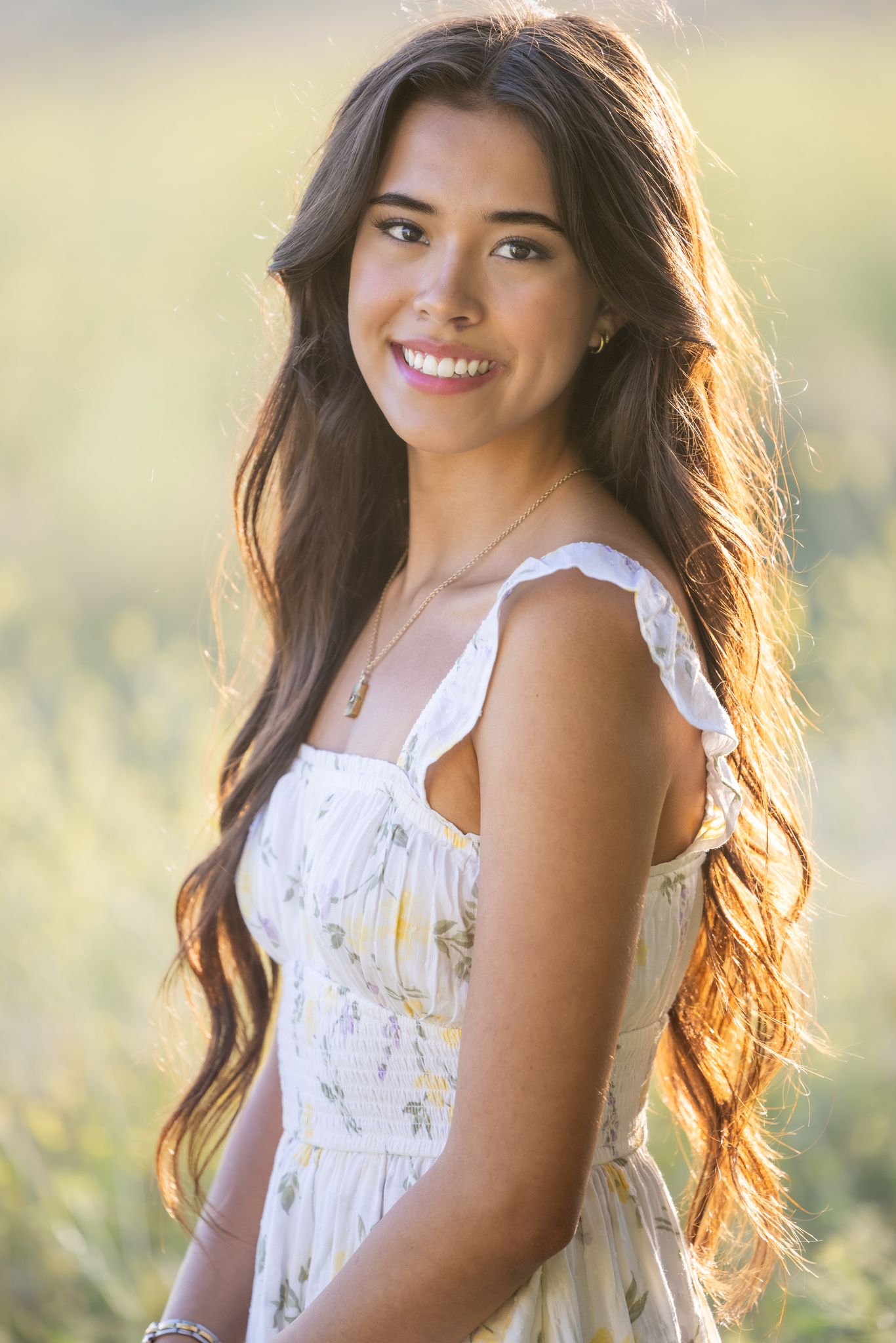 A person in a white sundress poses in a sunlit field with backlit hair creating a warm, ethereal glow.