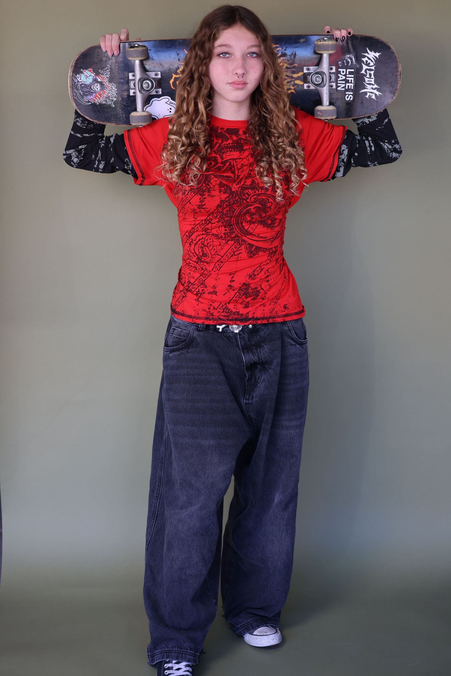 skater girl headshot. Standing pose in red top and wide-leg jeans showing skateboard.
