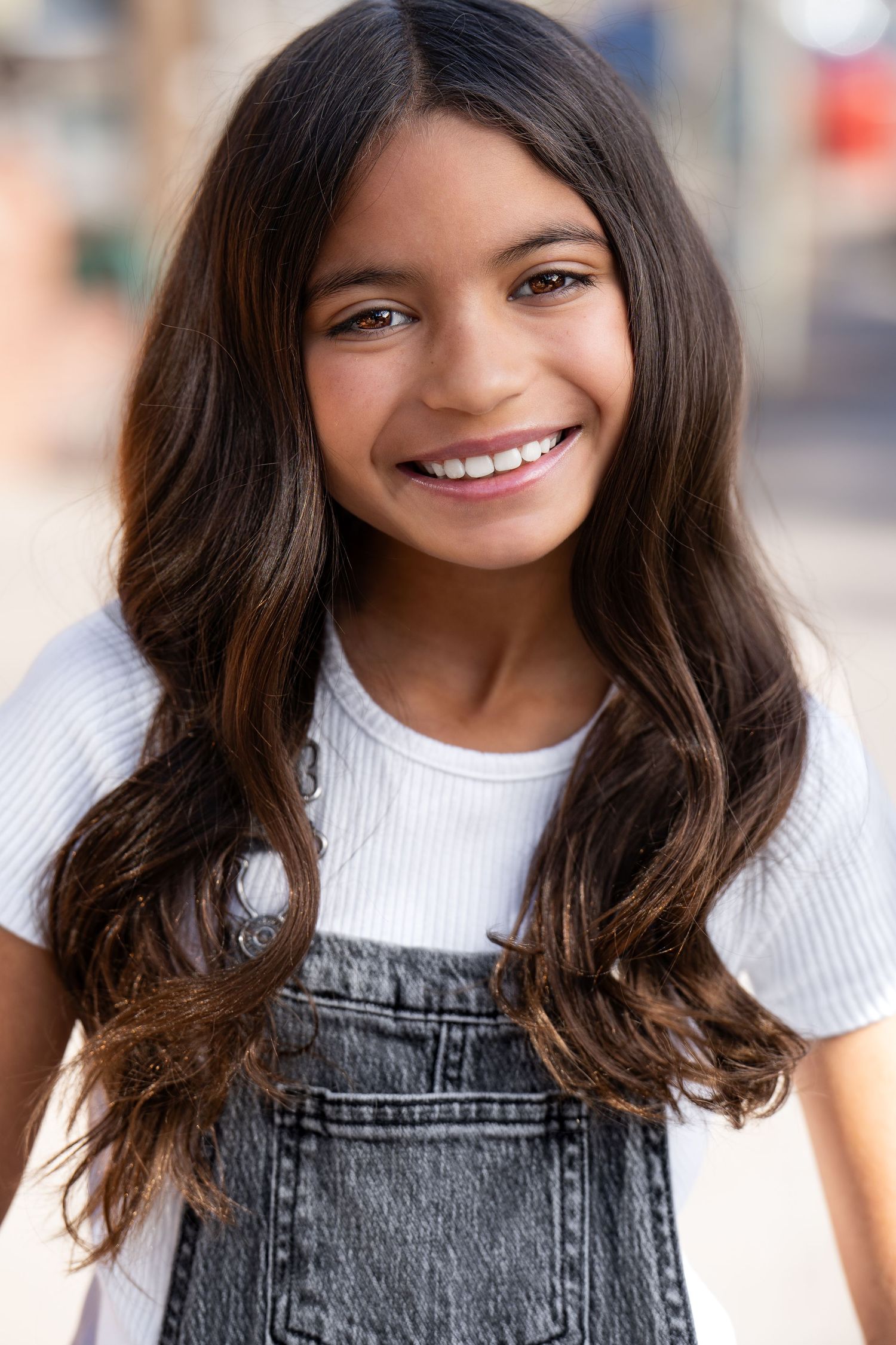 Smiling model wearing denim overalls and white t-shirt in outdoor setting.