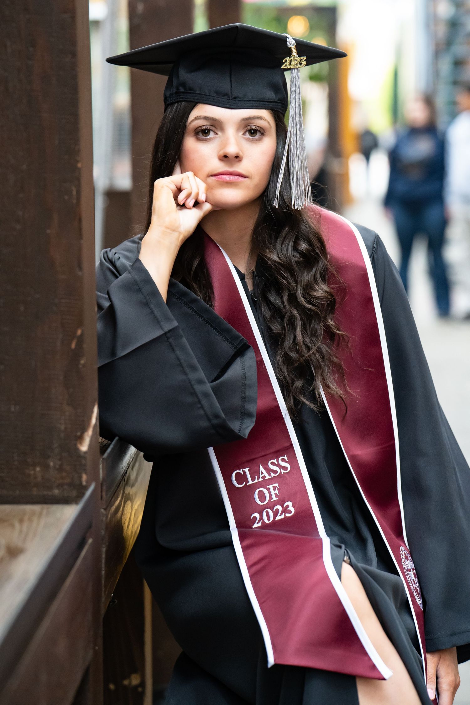 Graduate in black cap and burgundy gown poses for graduation photos with playful expressions.