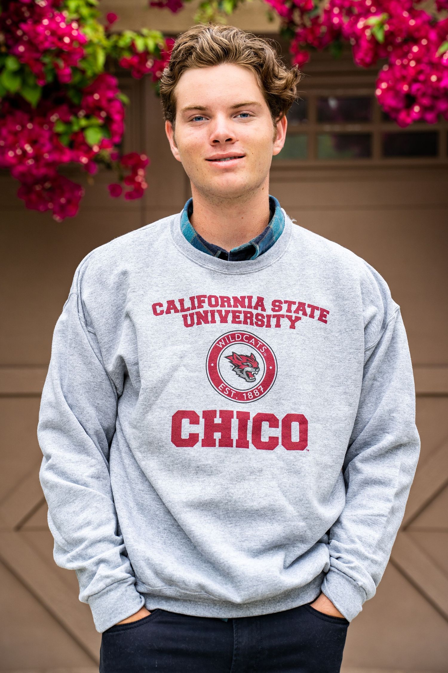 A person wearing a gray California State Chico University sweatshirt stands in front of pink flowers.