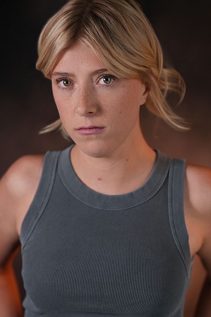 Young blonde woman with freckles wearing a gray ribbed tank top, posing for a professional headshot photo.
