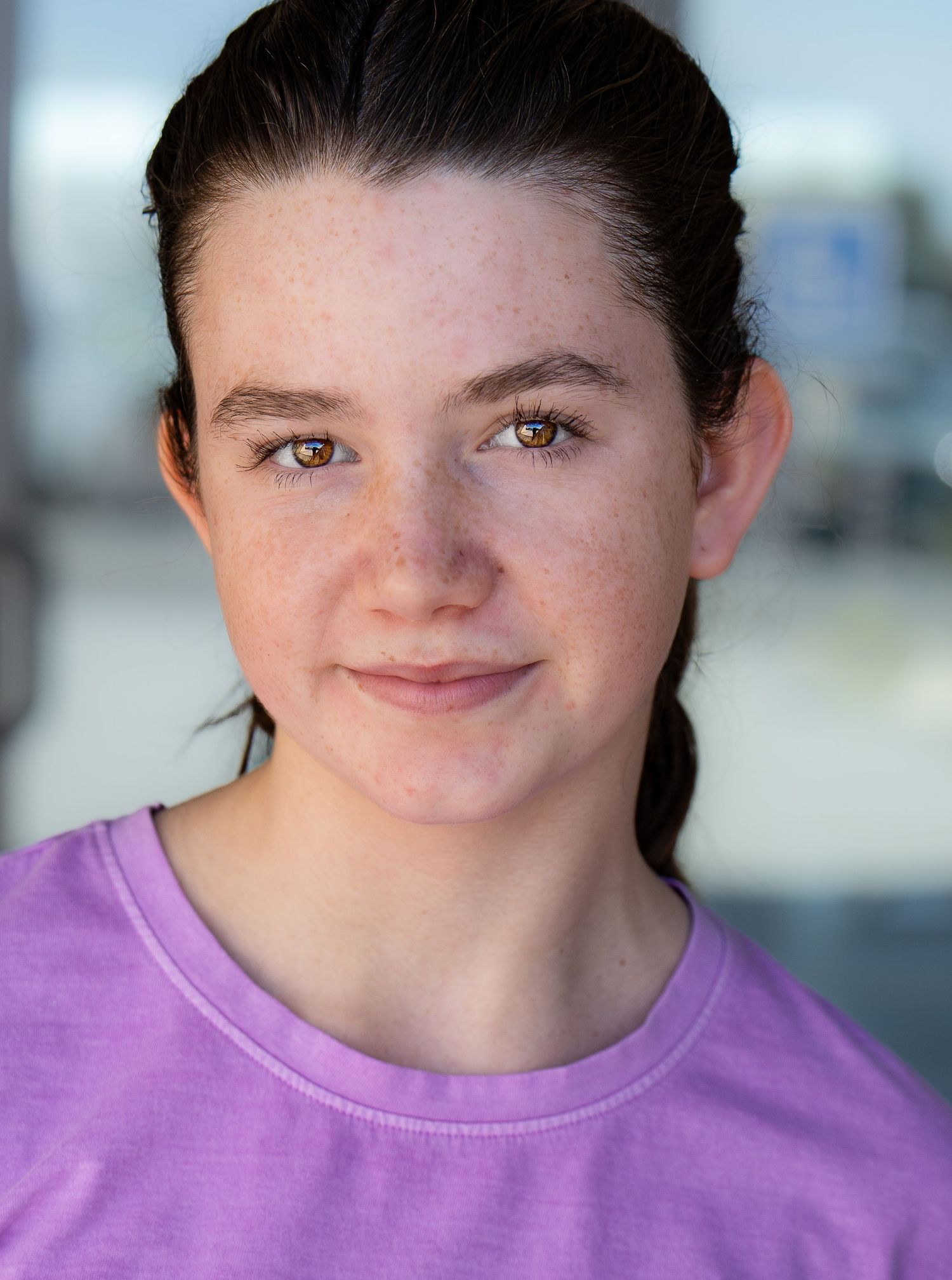 A person wearing a purple t-shirt smiling into the camera with a blurred background. headshot