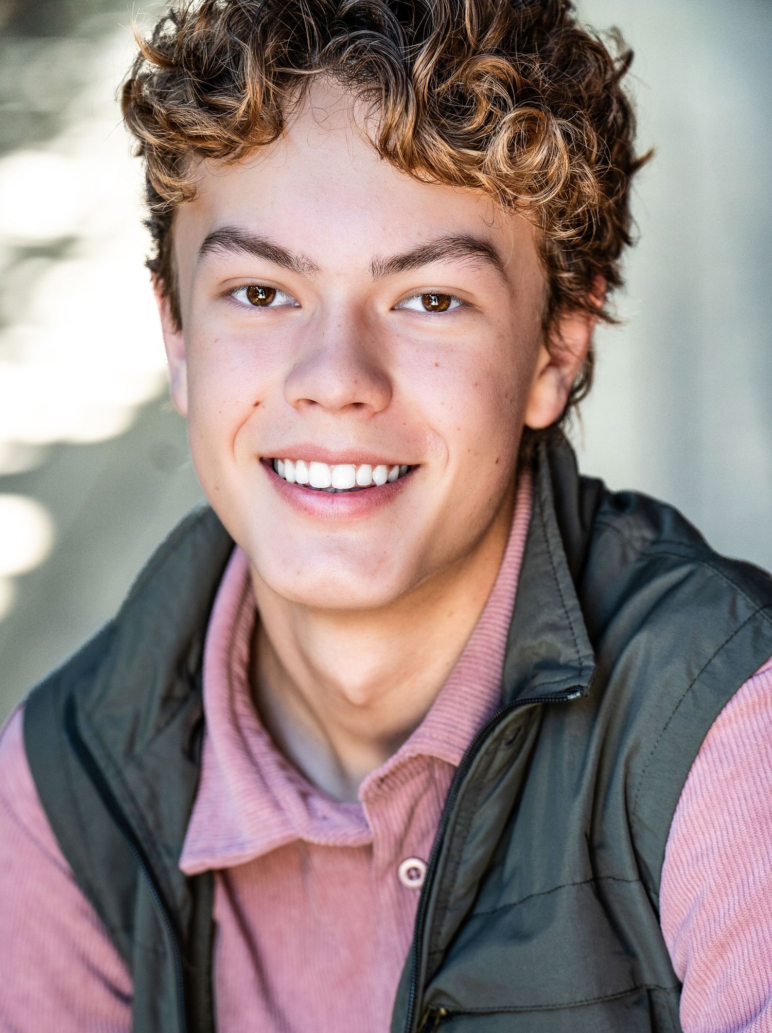 Professional studio headshots in black jacket and pink shirt showing warm expressions with golden curly hair.