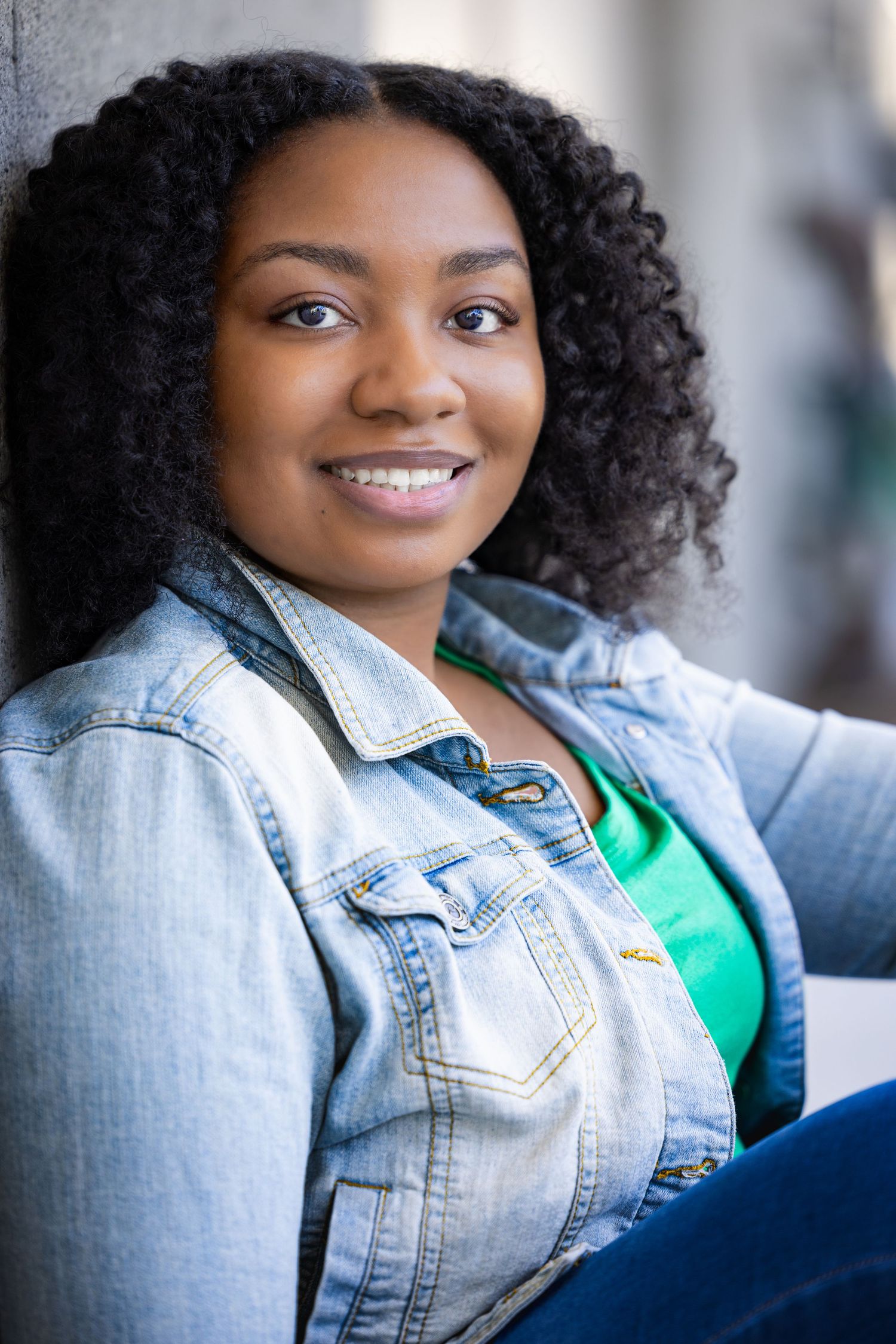 Cheerful poses in denim jacket and green top with natural lighting.