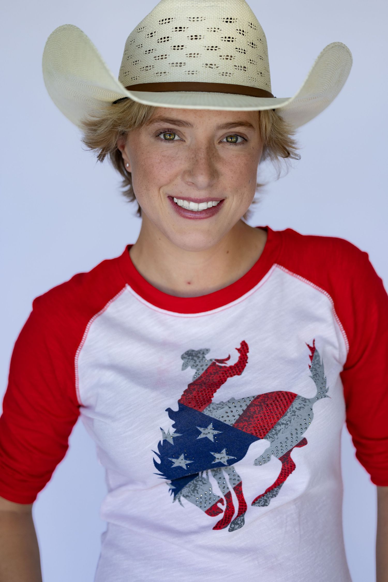 cowgirl headshot a white cowboy hat and patriotic t-shirt with red sleeves featuring an eagle design.