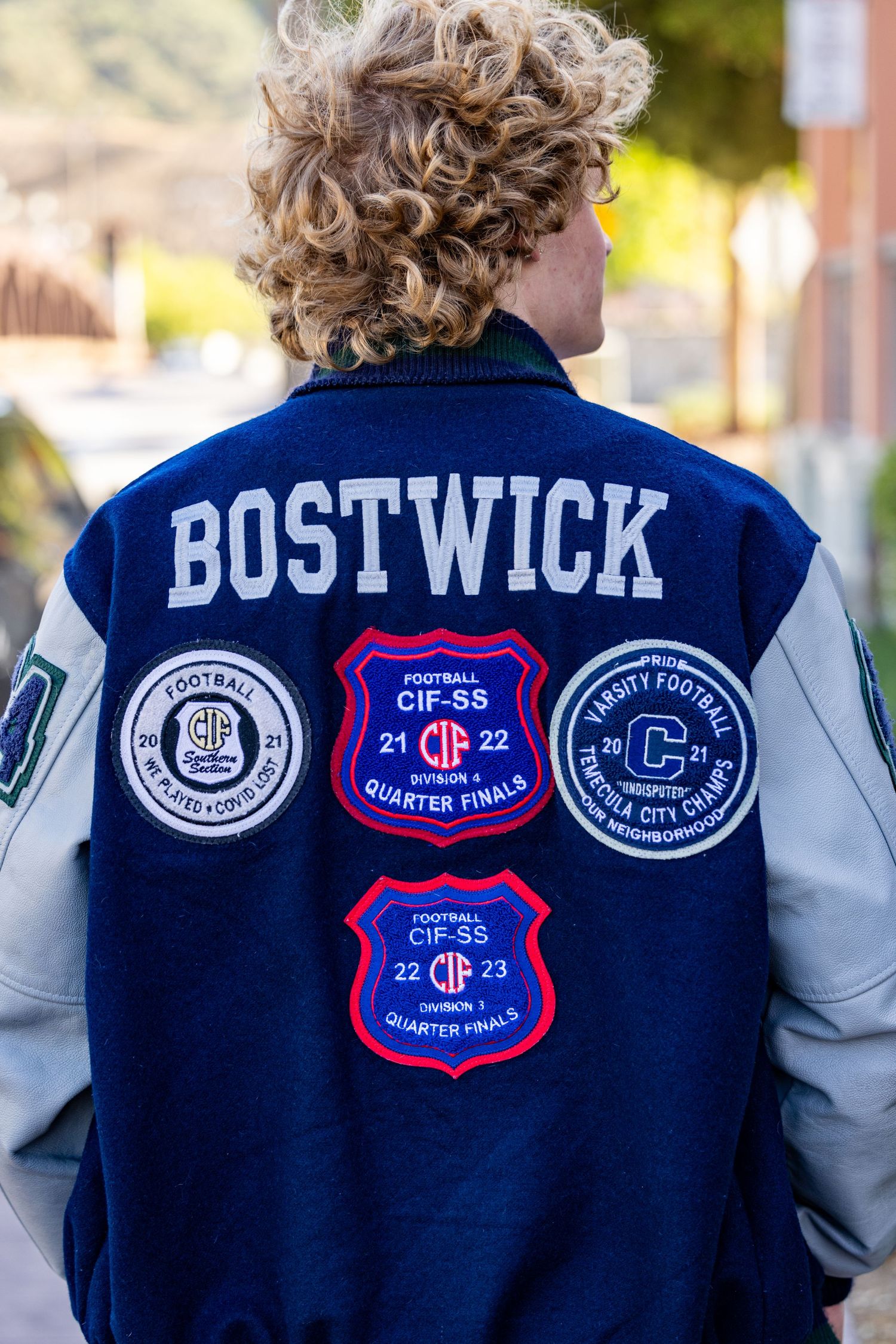 Close-up view of navy blue varsity jackets with embroidered patches and Bostwick lettering on the back.