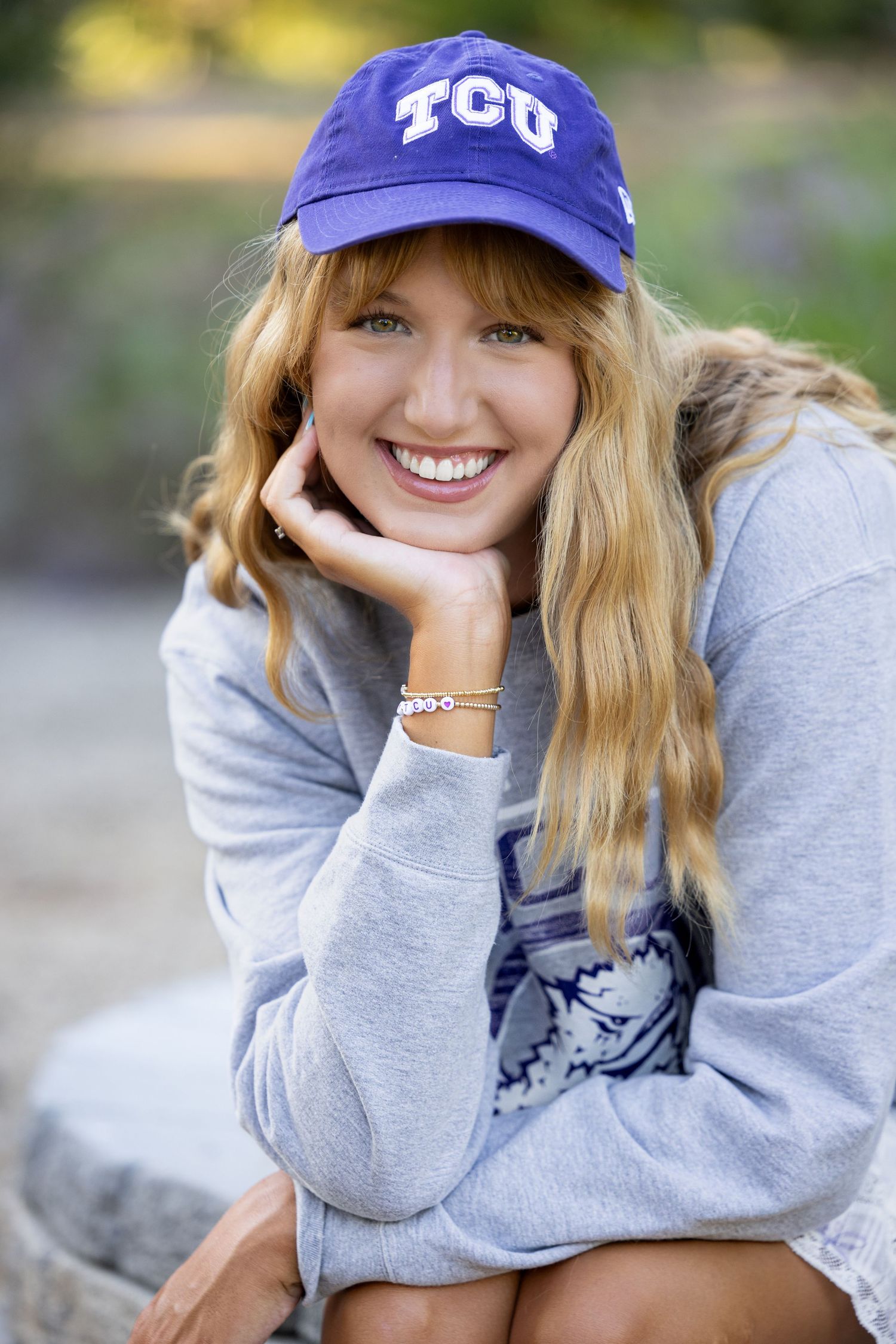 A person in a gray sweatshirt and purple TCU baseball cap smiles while posing outdoors.
