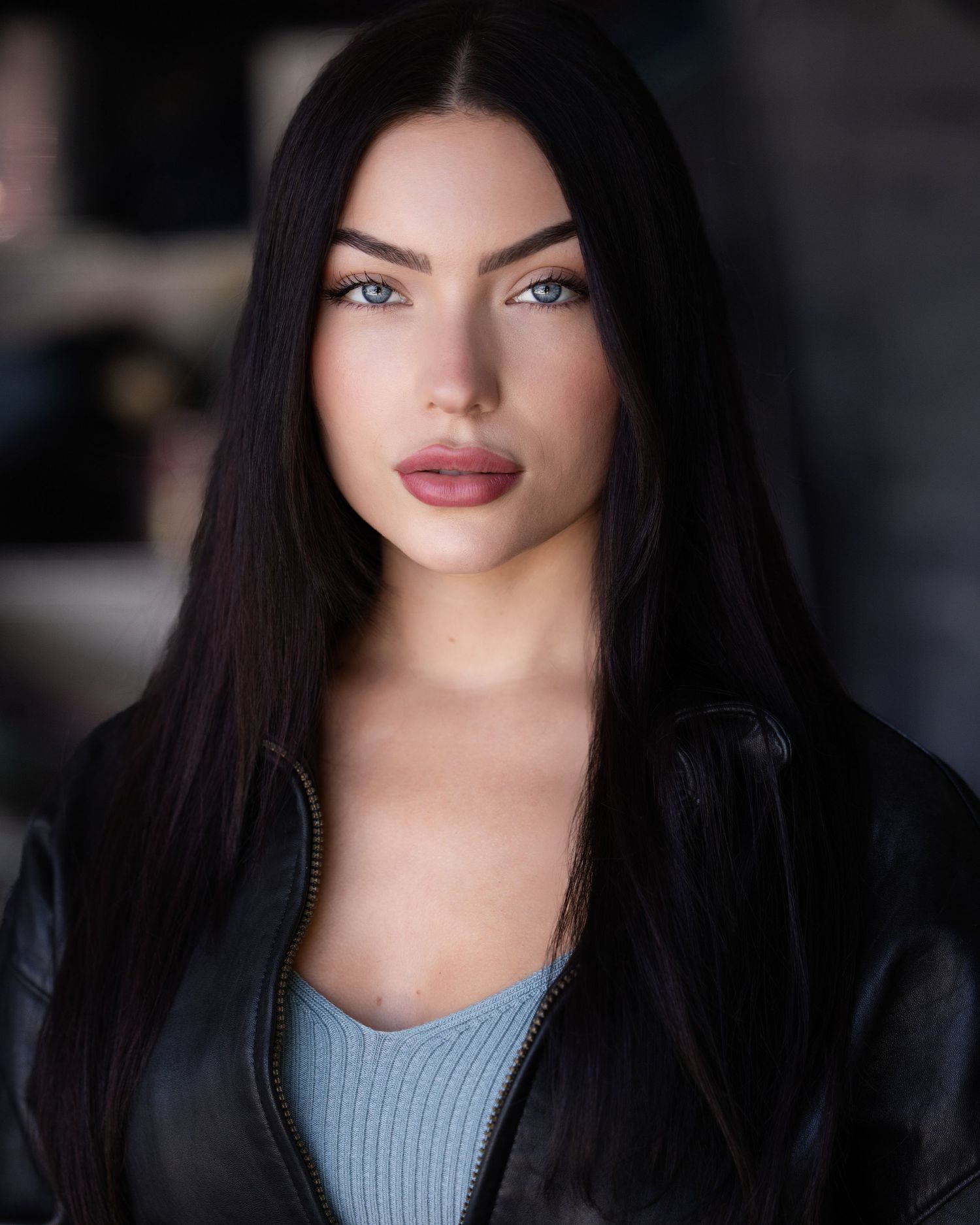 Portrait with long dark hair wearing light blue top against dark background.